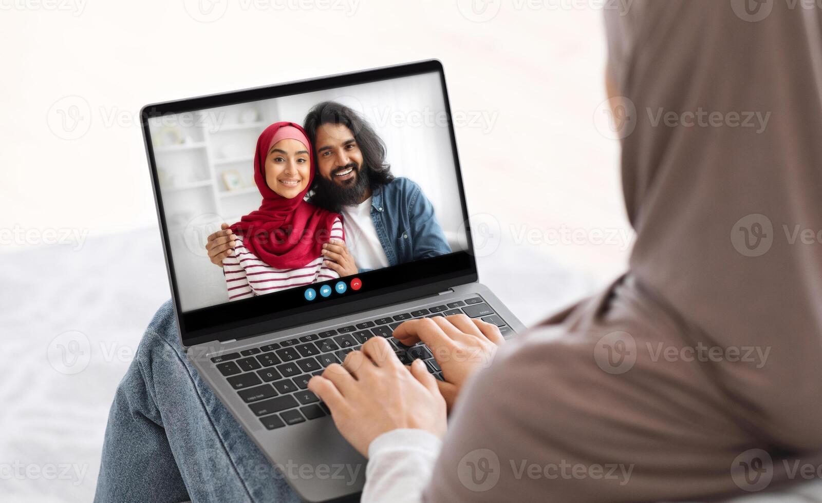 A woman in a headscarf smiles while chatting with her friends, capturing a moment of connection and laughter from the comfort of her home on a bright afternoon. photo