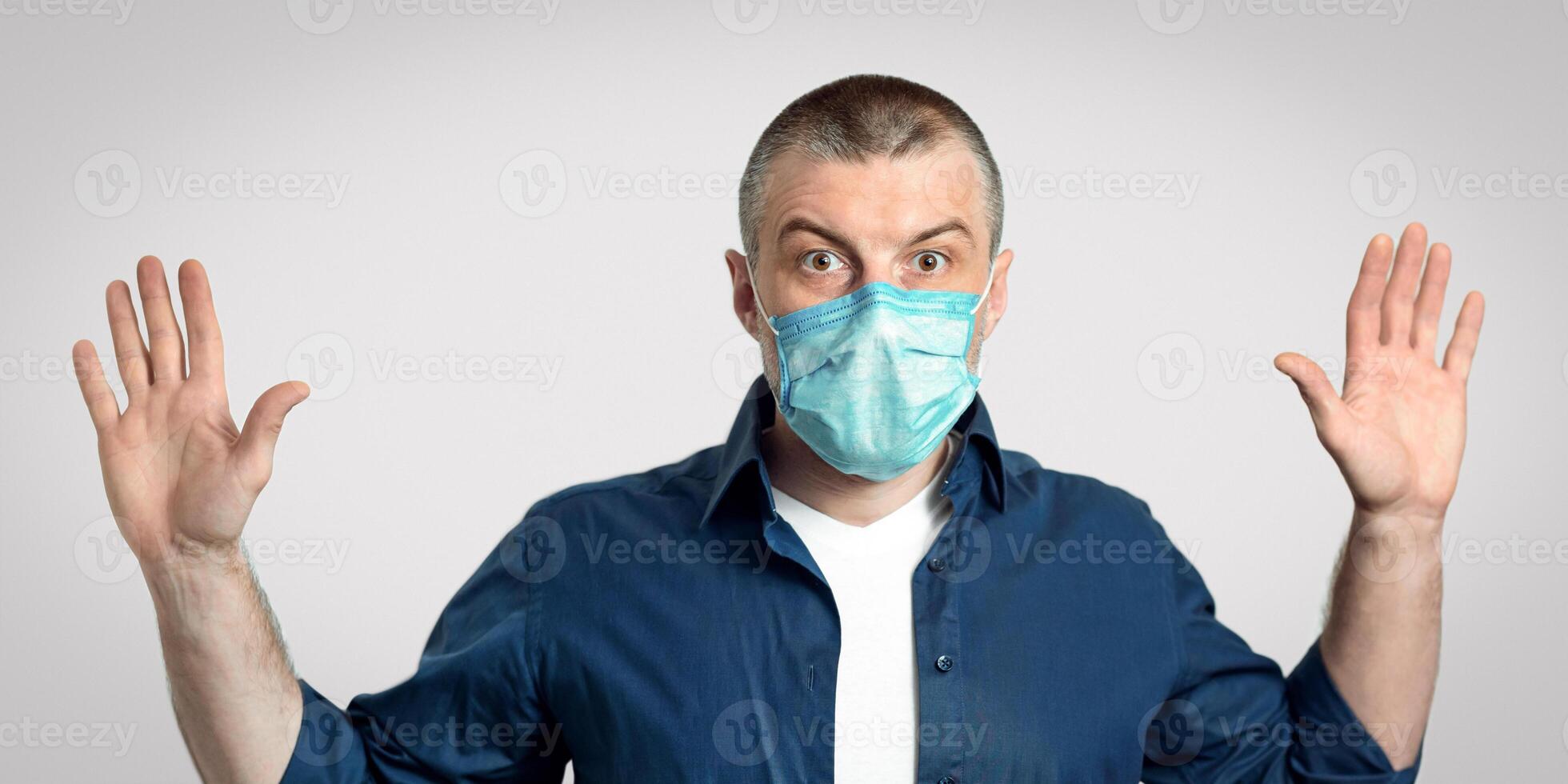 Man In Medical Mask Raising Hands Posing On Gray Background During Covid-19 Pandemic Outbreak. Studio Shot, Panorama photo