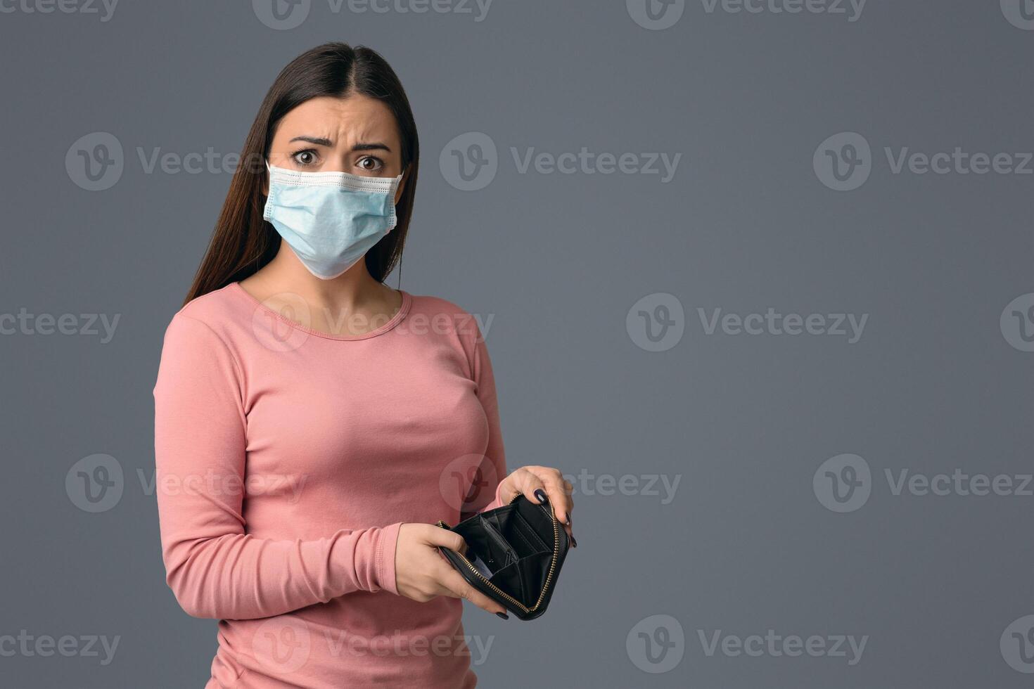 Coronacrisis Concept. Portrait of concerned young woman with empty wallet in hands, standing over light studio background and looking at camera photo