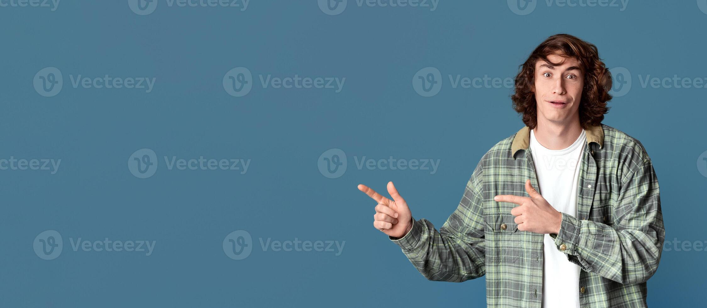 Surprised teenage guy pointing to empty space on turquoise studio background photo