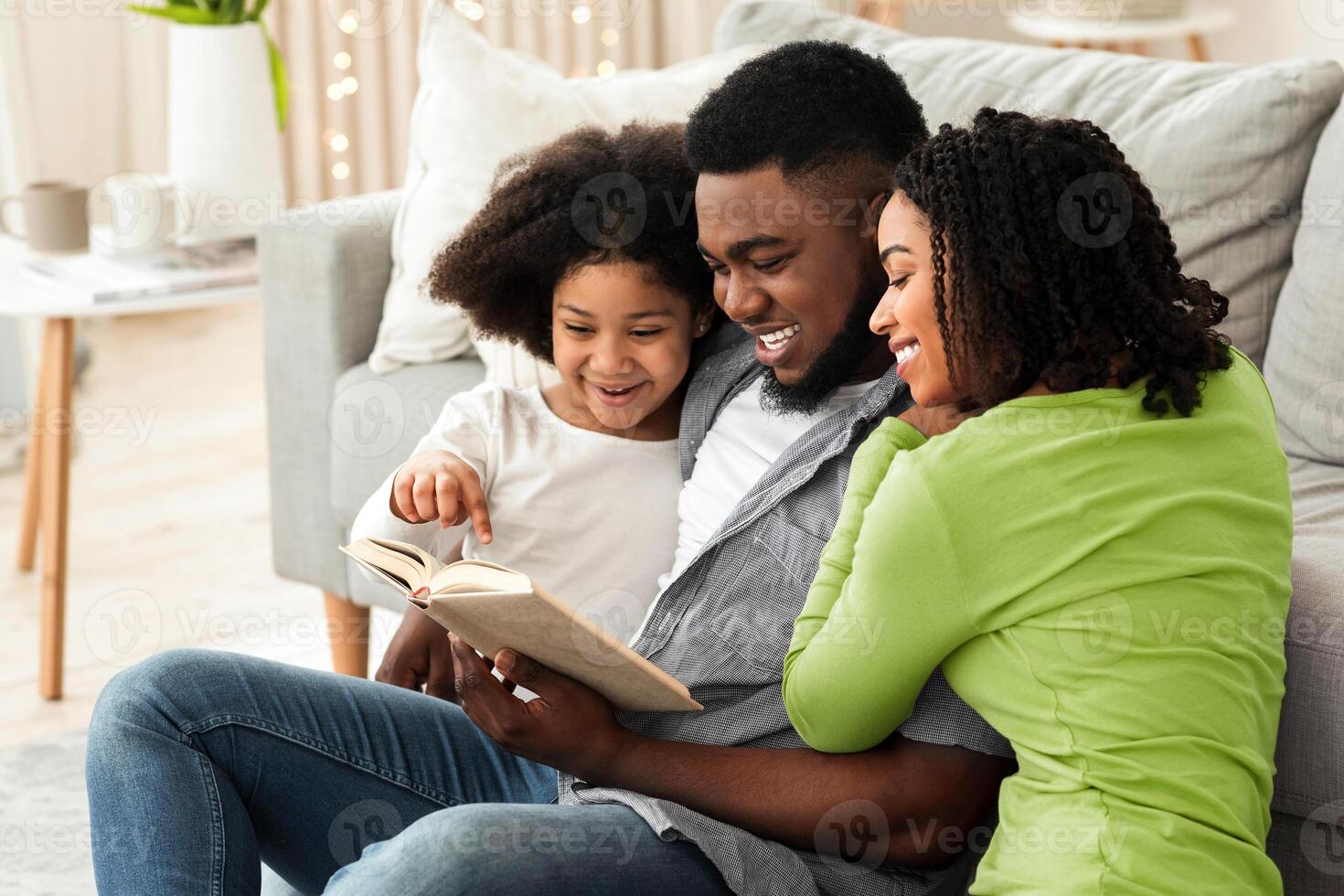 Happy black family reading book together, sitting on floor in living room, enjoying spending quarantine at home, bonding and smiling photo