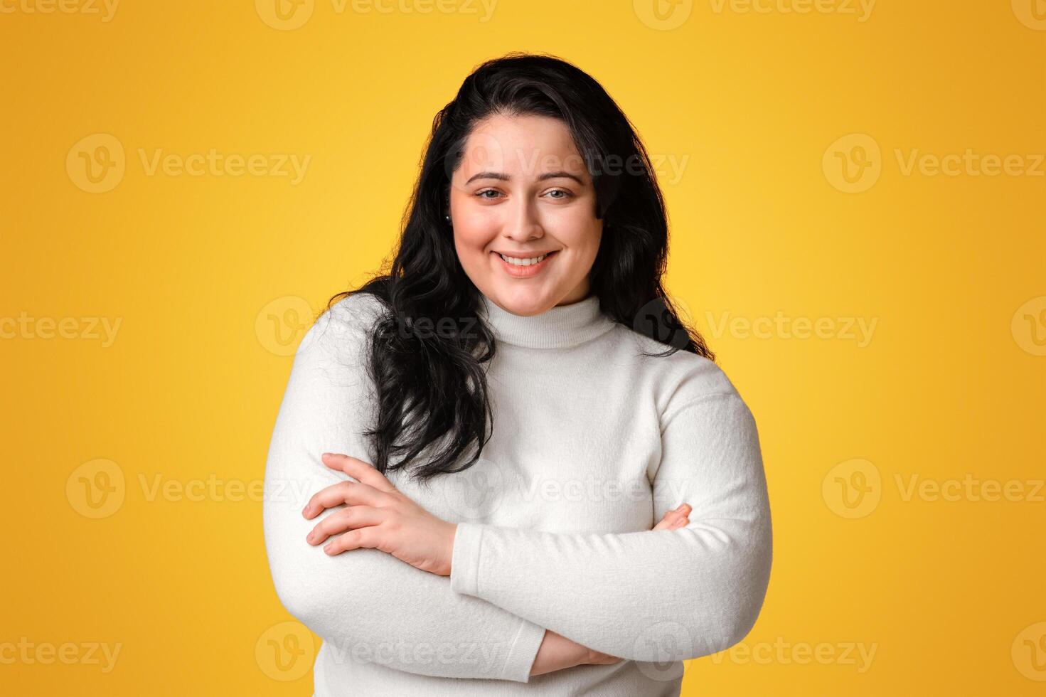 Body Positive. Young Plus Size Model Girl Posing With Folded Arms Over Yellow Background And Smiling At Camera photo