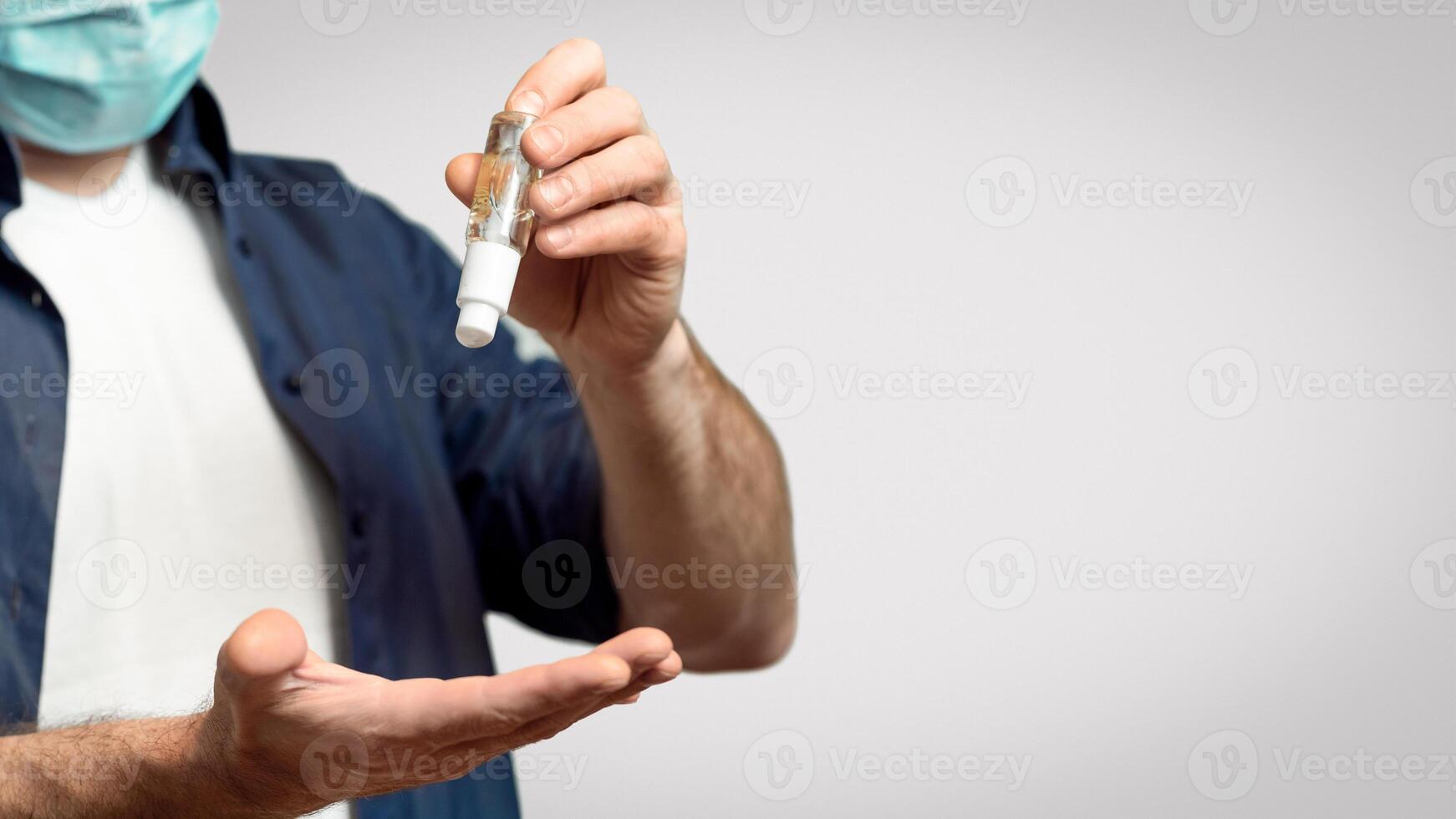 Unrecognizable Man Disinfecting Hands With Medical Sanitizer Gel For Coronavirus Prevention Standing Over Gray Studio Background. Cropped photo