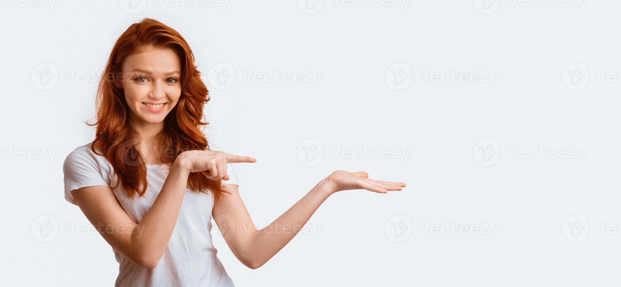 Look Here. Teen Girl Pointing Finger Holding Invisible Object On Hand Posing Over White Studio Background. Panorama, Empty Space photo