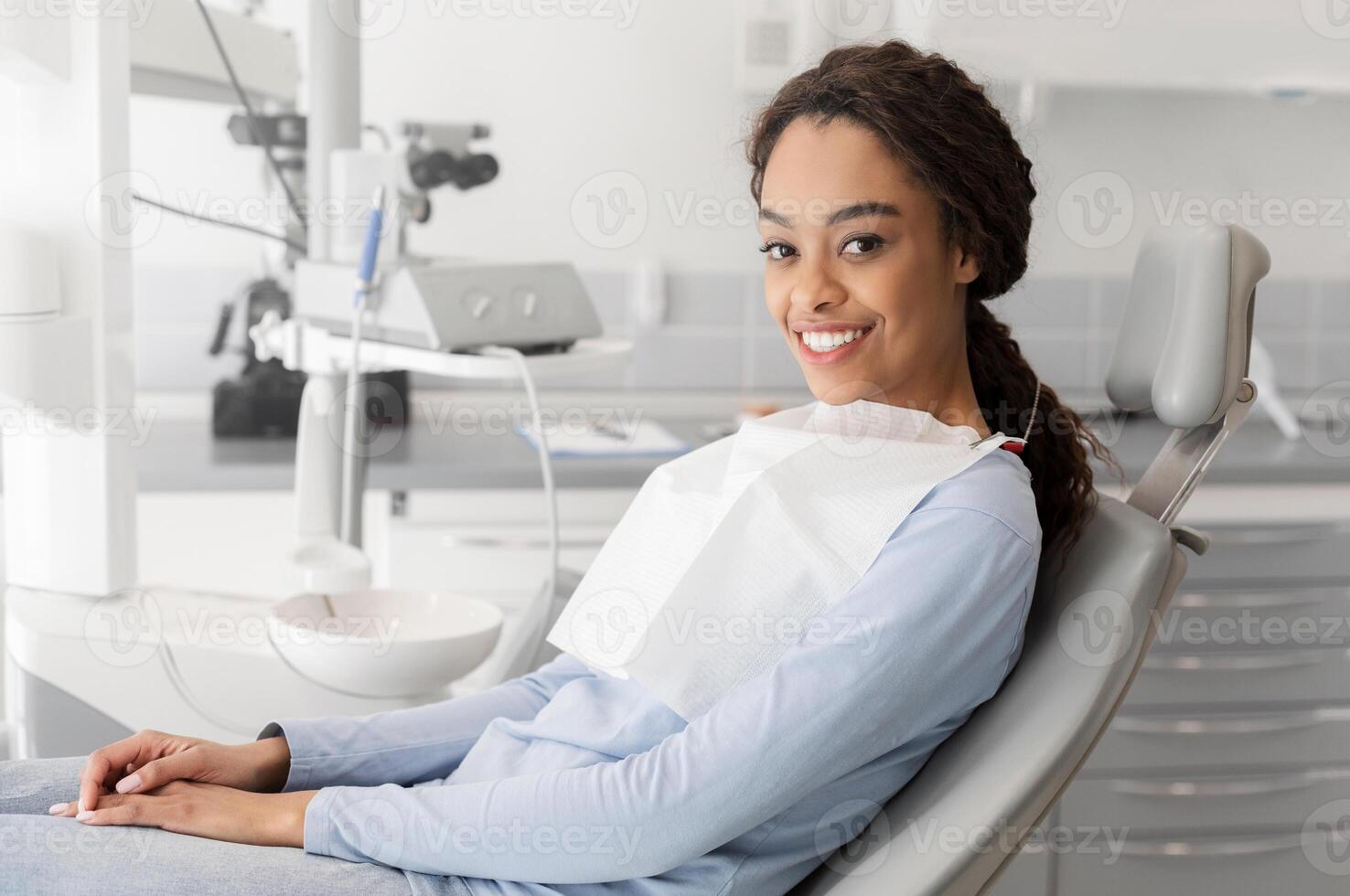 Young black lady sitting in dentist chair and smiling at camera, copy space photo