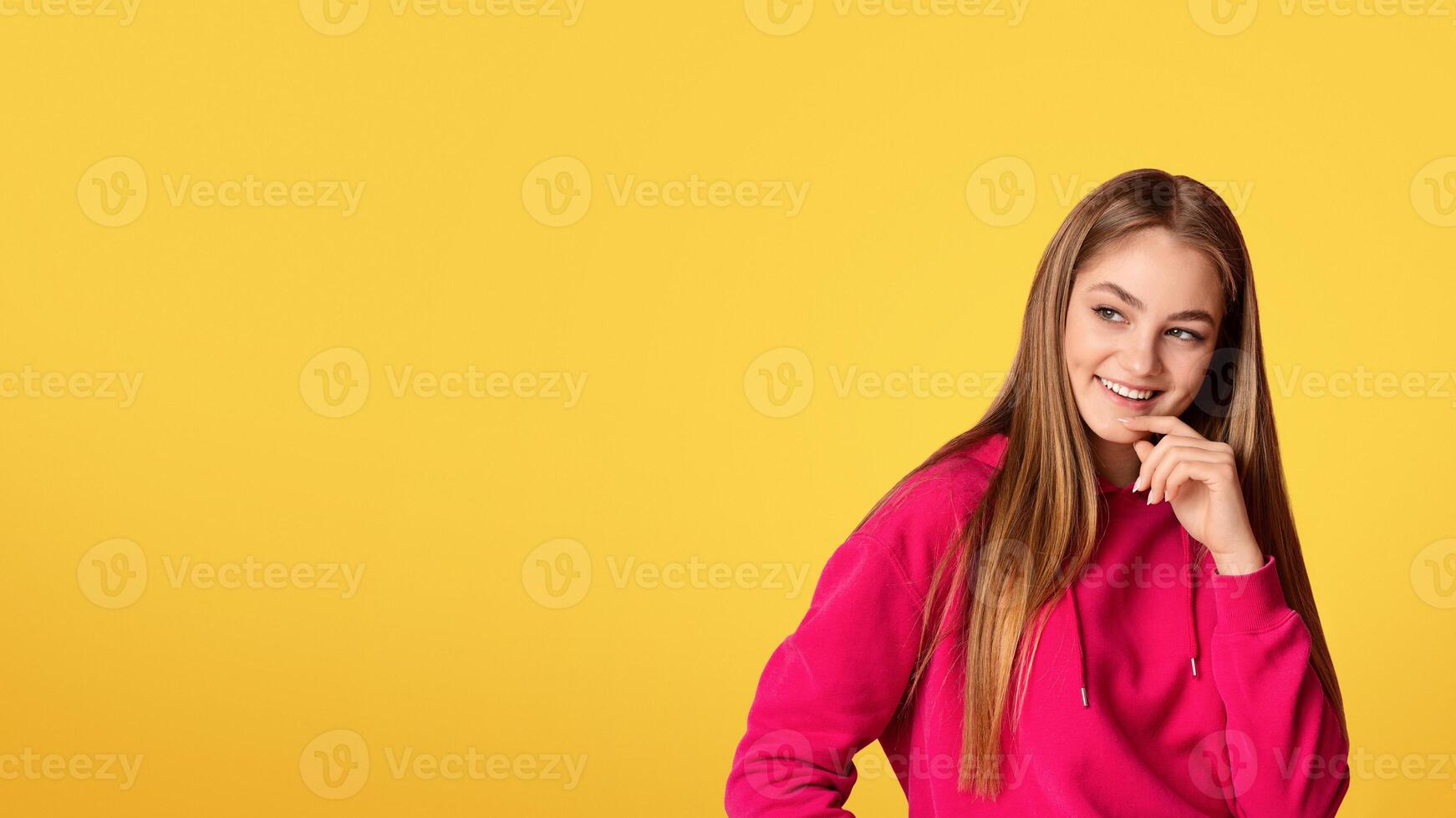 Flirting smiling teen girl touches her chin and looks at an empty space, panorama, studio shot photo