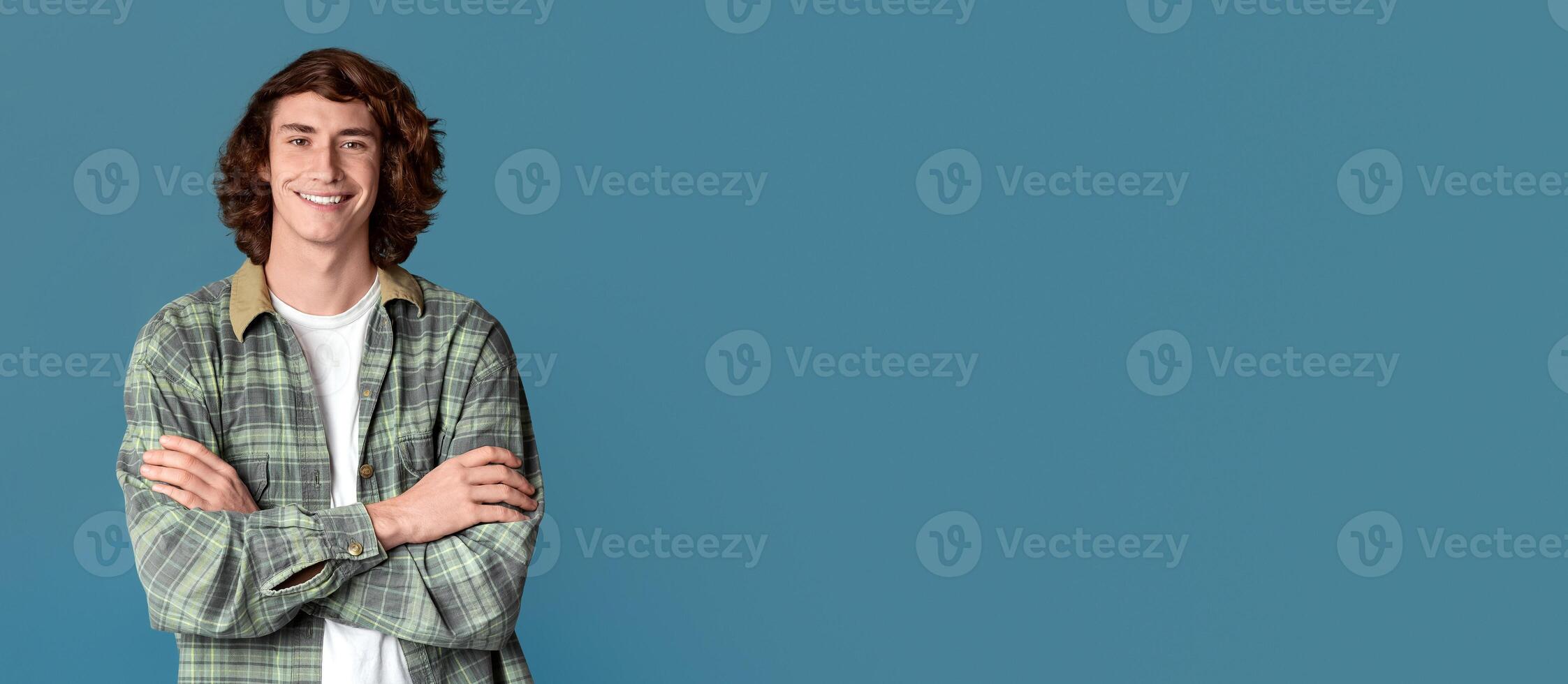 Happy millenial guy with curly hair crossing his arms on turquoise background photo