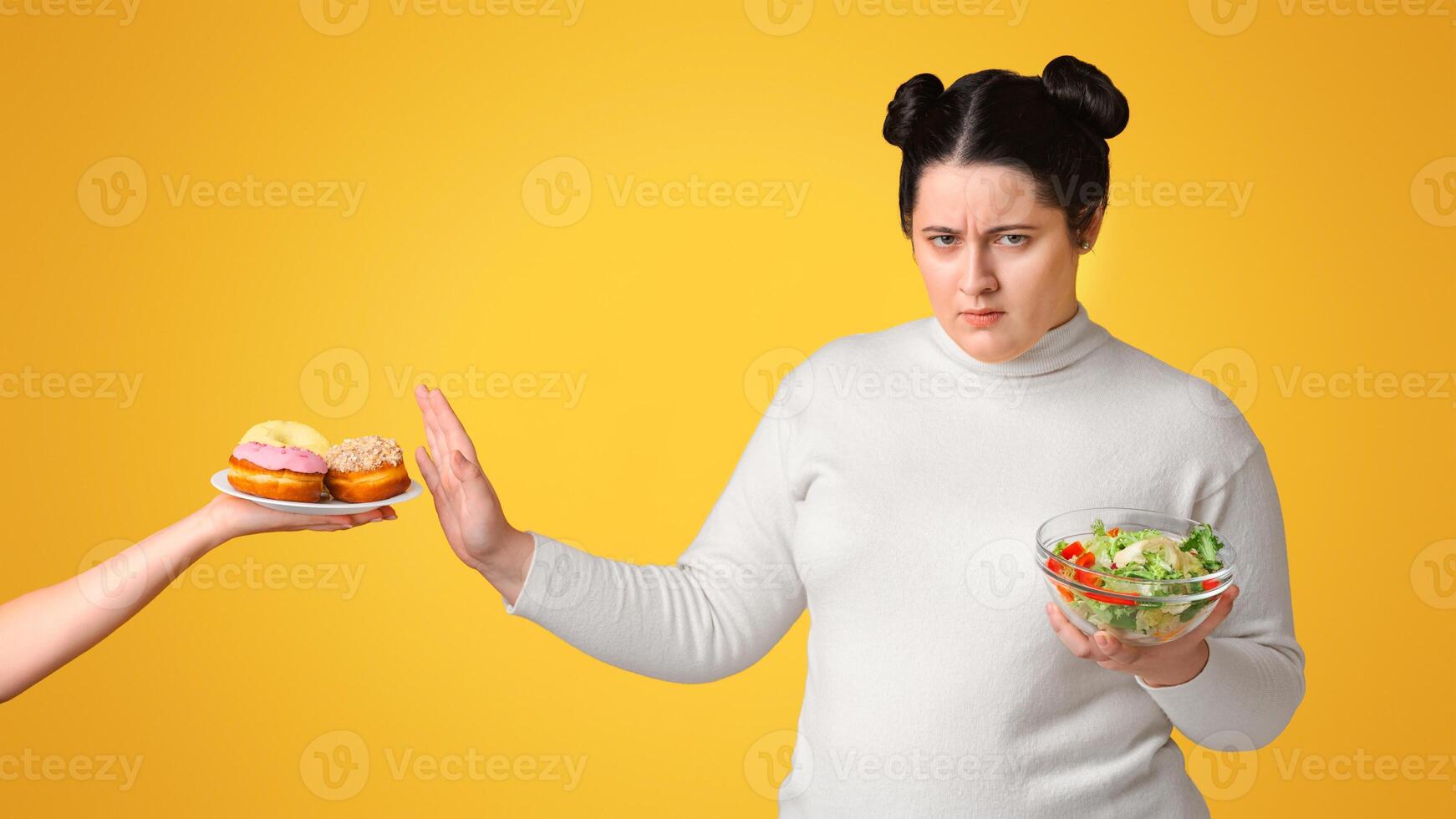 Say No To Obesity. Annoyed Plump Woman Showing Stop Gesture To Offered Plate With Donuts And Eating Fresh Vegetable Salad, Yellow Background photo