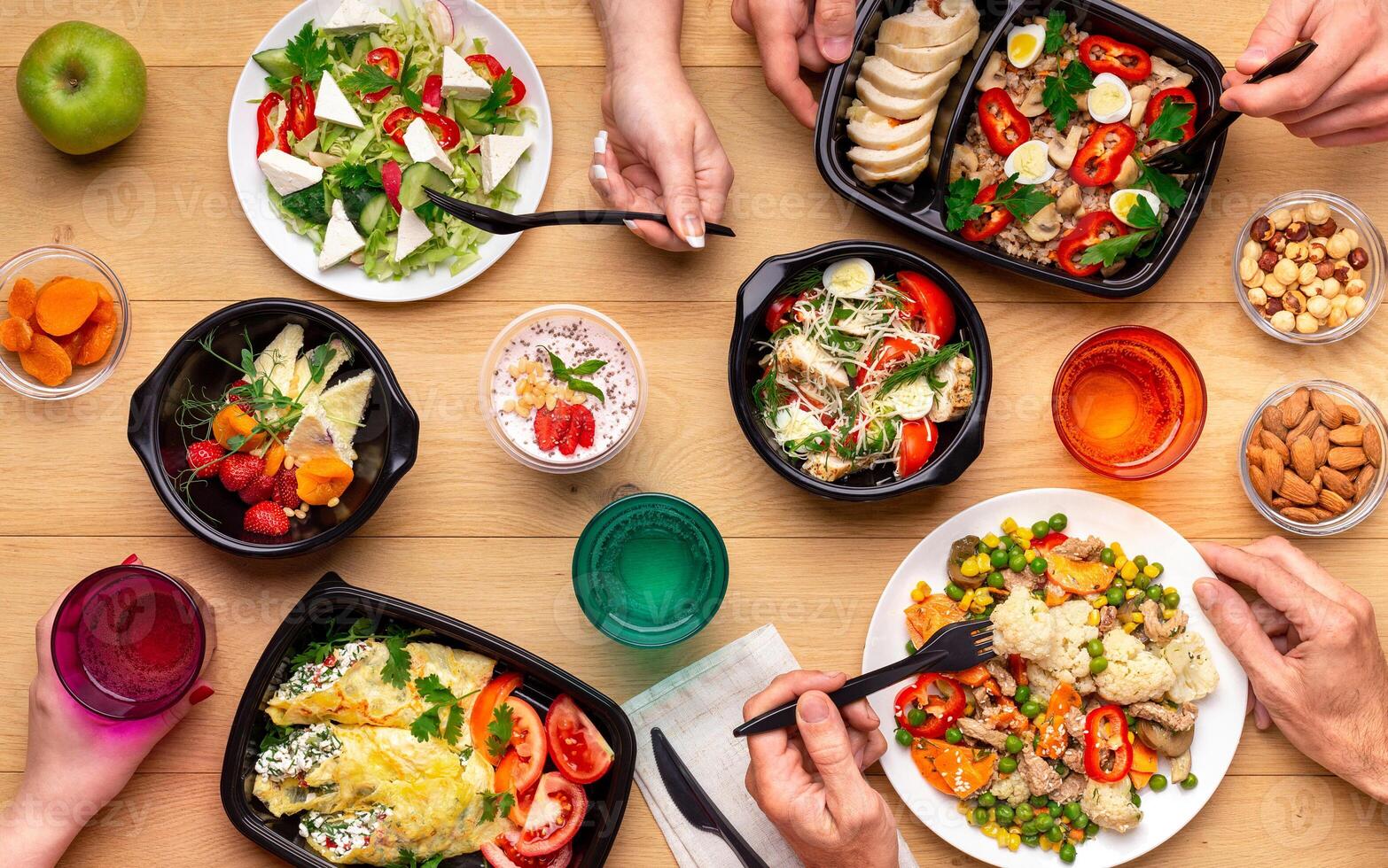 Healthy lunch time at office workplace. Four people eating healthy meals from take away lunch boxes and plates at wooden table. concept, top view photo