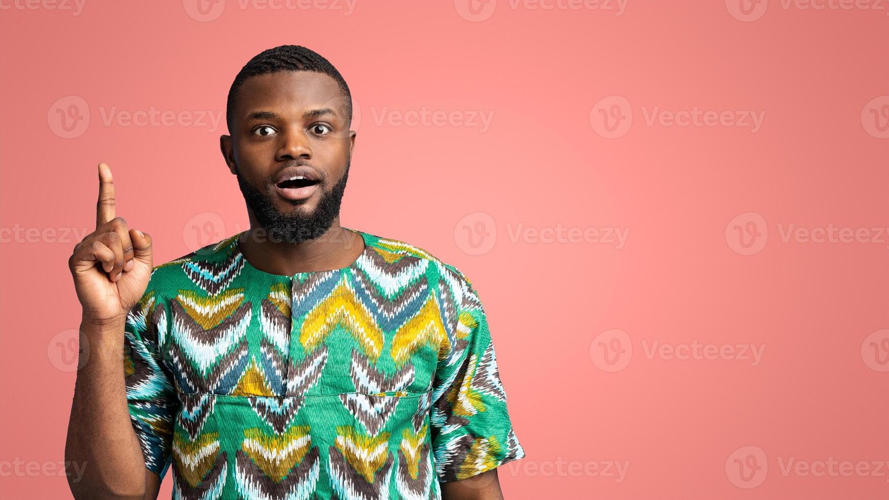 Shocked black man in traditional costume having great idea, pointing finger up, got problem solution, pink studio background, copy space. Emotional african american guy got idea, eureka photo