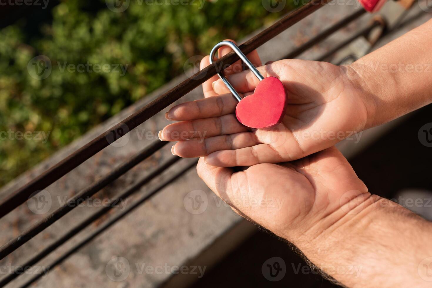 A couple shares a romantic moment as they place a heart-shaped padlock on a railing, symbolizing their love. This heartfelt gesture captures their connection in a serene outdoor setting. photo