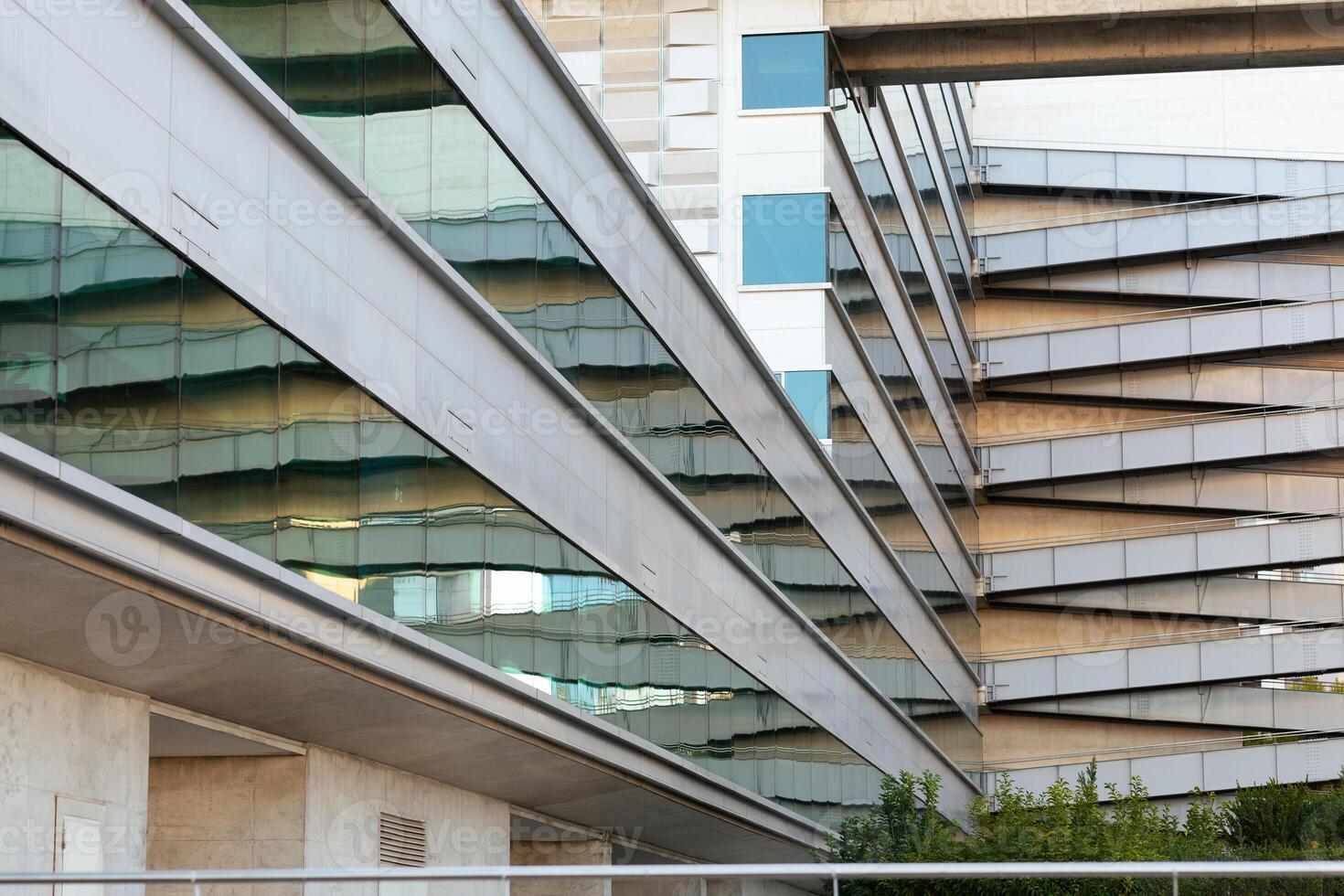 A contemporary building features sleek glass panels reflecting its geometric design. The architecture showcases innovative lines and textures against a clear urban backdrop. photo