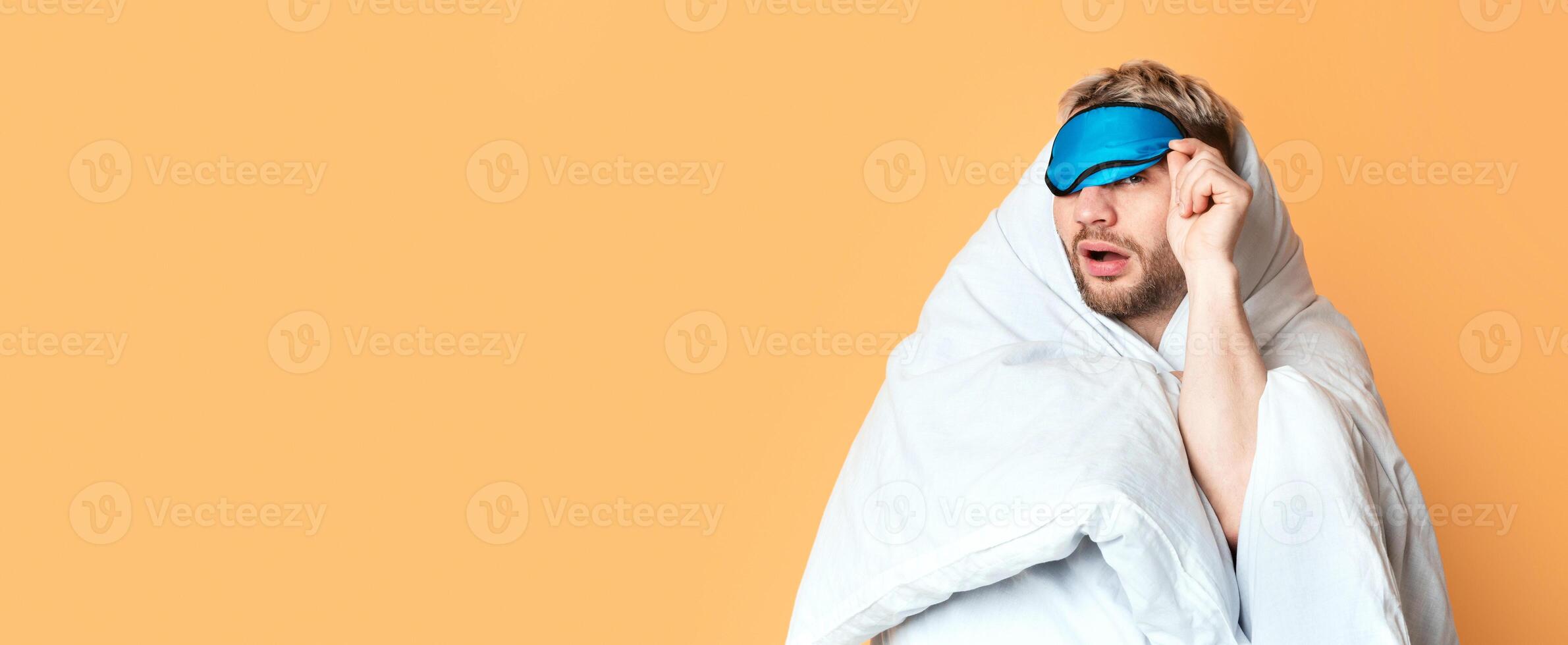 Funny guy wrapped in blanket takes off his sleep mask and squints photo