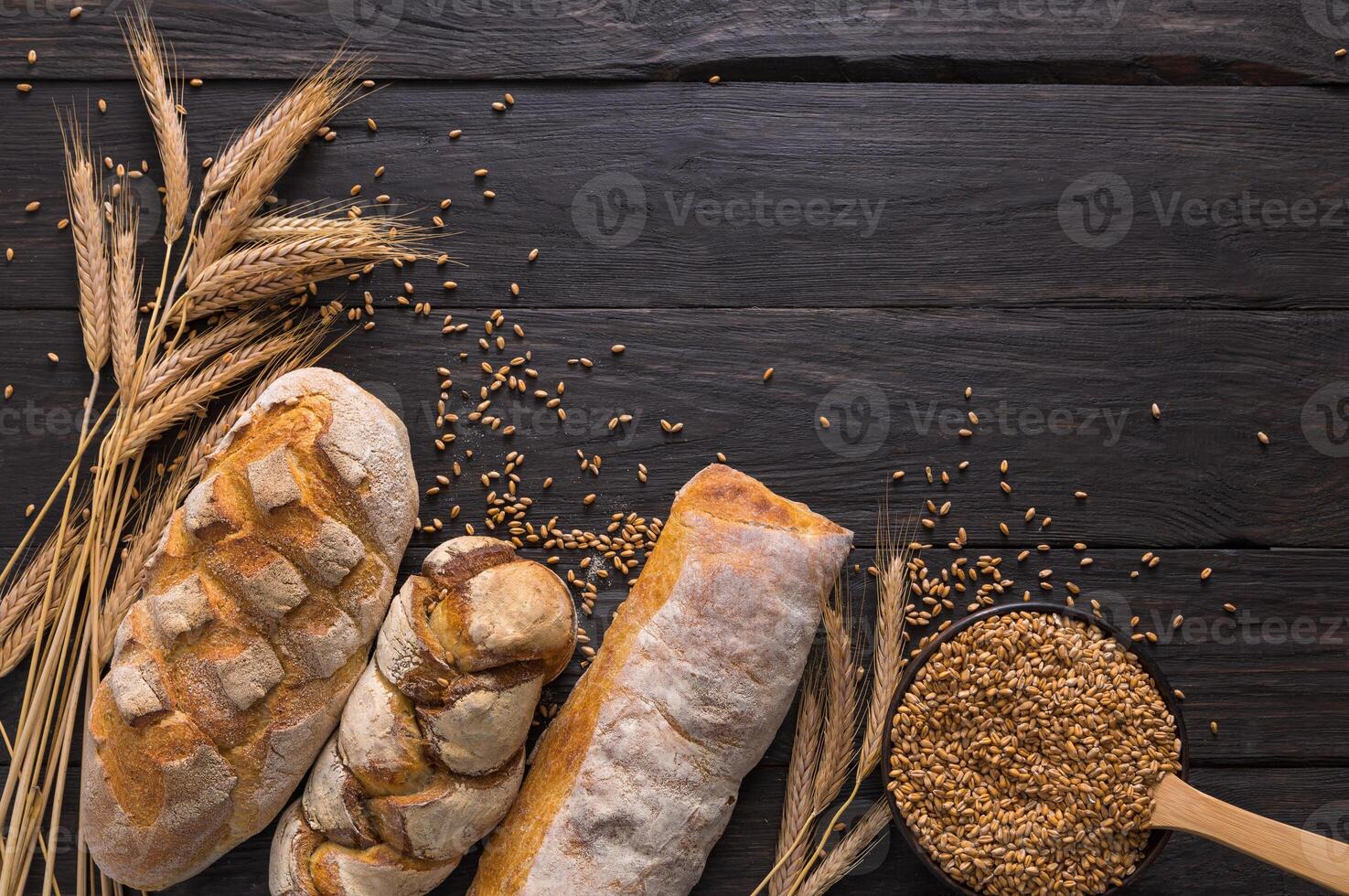 Bread border on wood with copy space background. Brown and white whole grain loaves still life composition with wheat ears scattered around. Bakery and grocery food store concept. photo