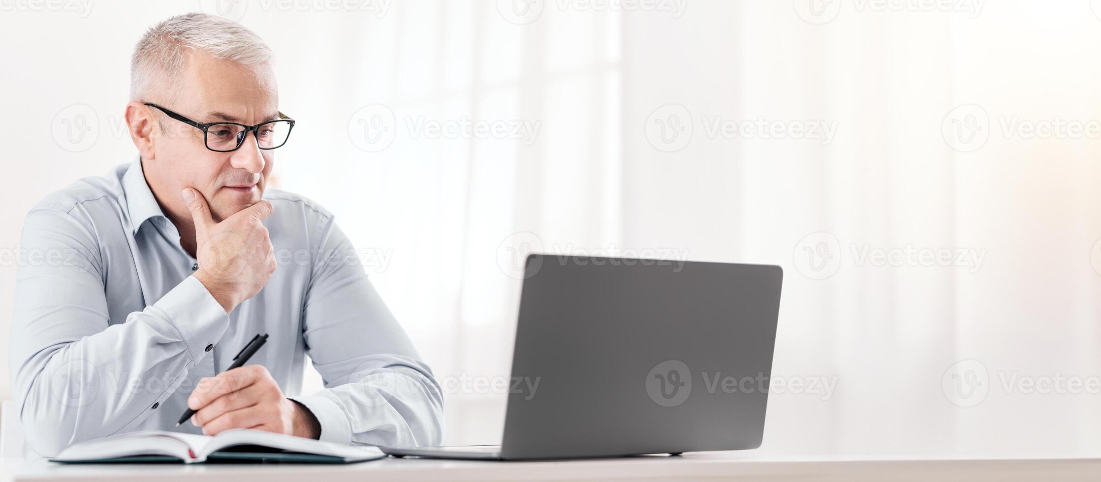 Pensive Mature Man Using Laptop And Writing In Notepad Sitting At Desk At Home, Free Space photo