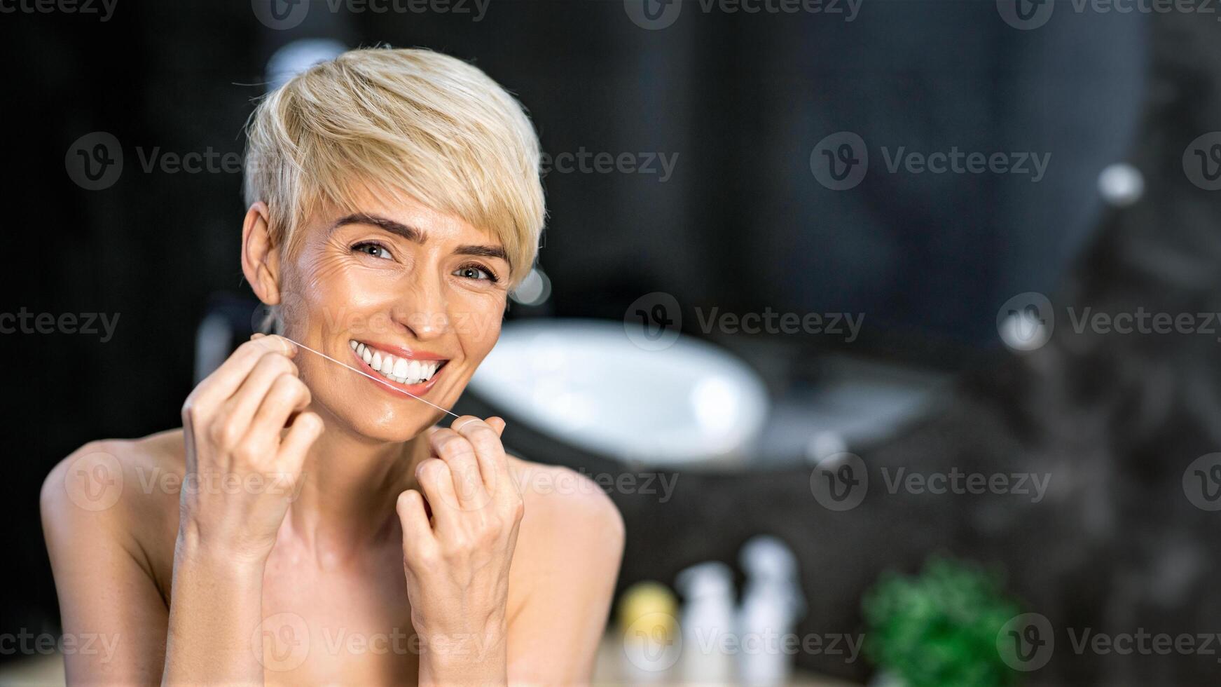 Tooth Care Routine. Cheerful Woman Flossing Her Teeth Standing In Bathroom At Home. Empty Space For Text photo