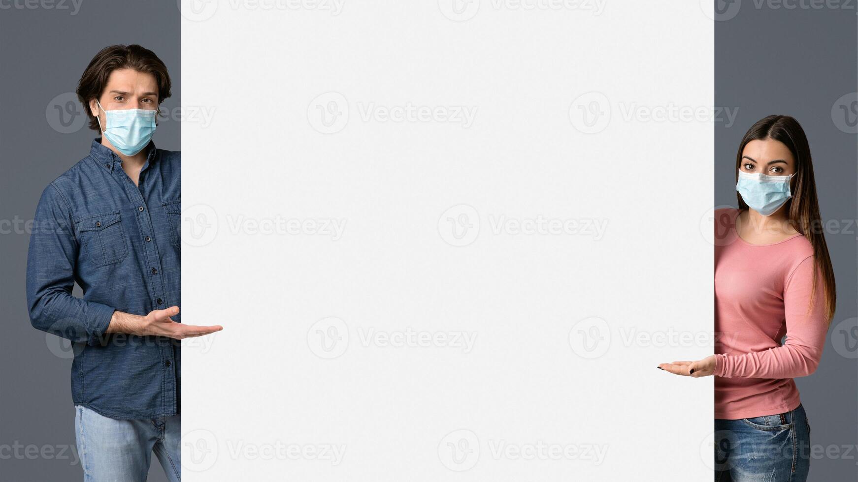 Young Couple In Medical Masks Pointing At White Advertisement Board With Open Palms, Standing Together Over Light Background, Free Place For Your Text photo