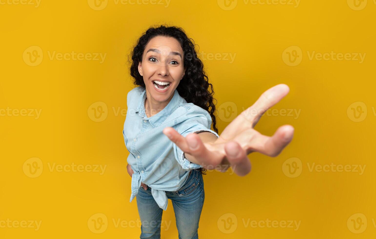 Excited young woman outstretching cupped hand, trying to grab or hold something invisible on her palm, giving it away or asking for something, orange yellow wall, copy space, above top high angle view photo
