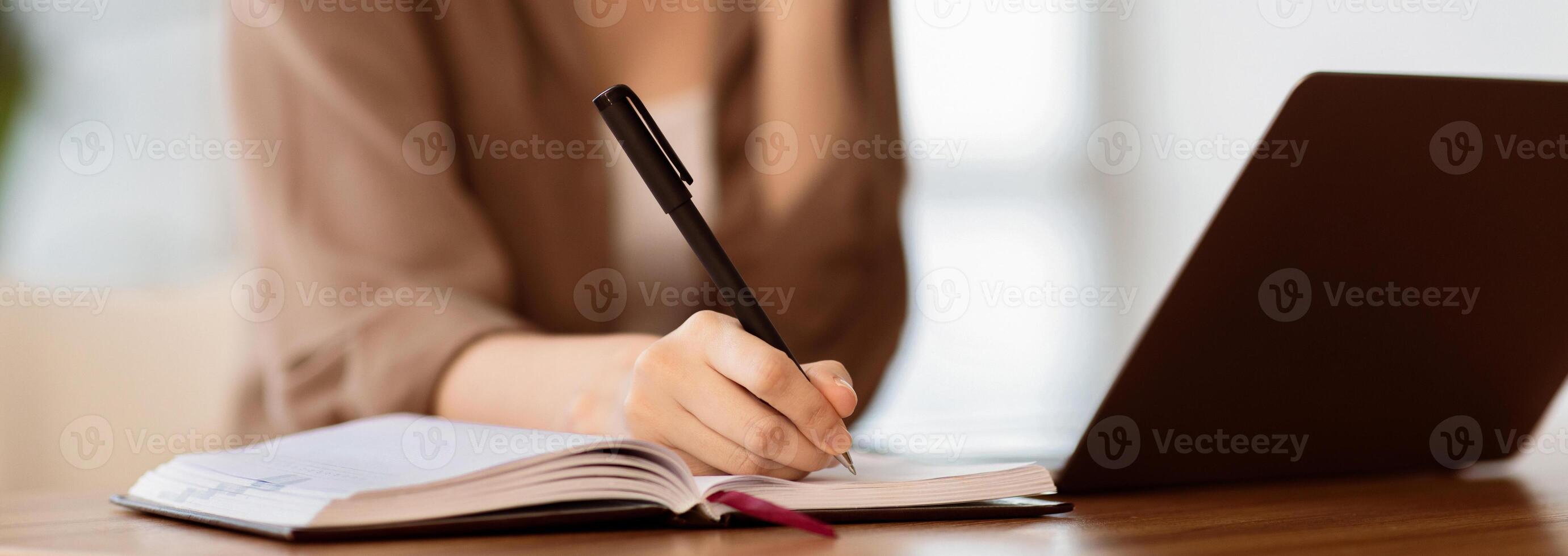 Taking Notes. Young secretary sitting at desk with laptop computer and talking on mobile phone, writing in notebook photo