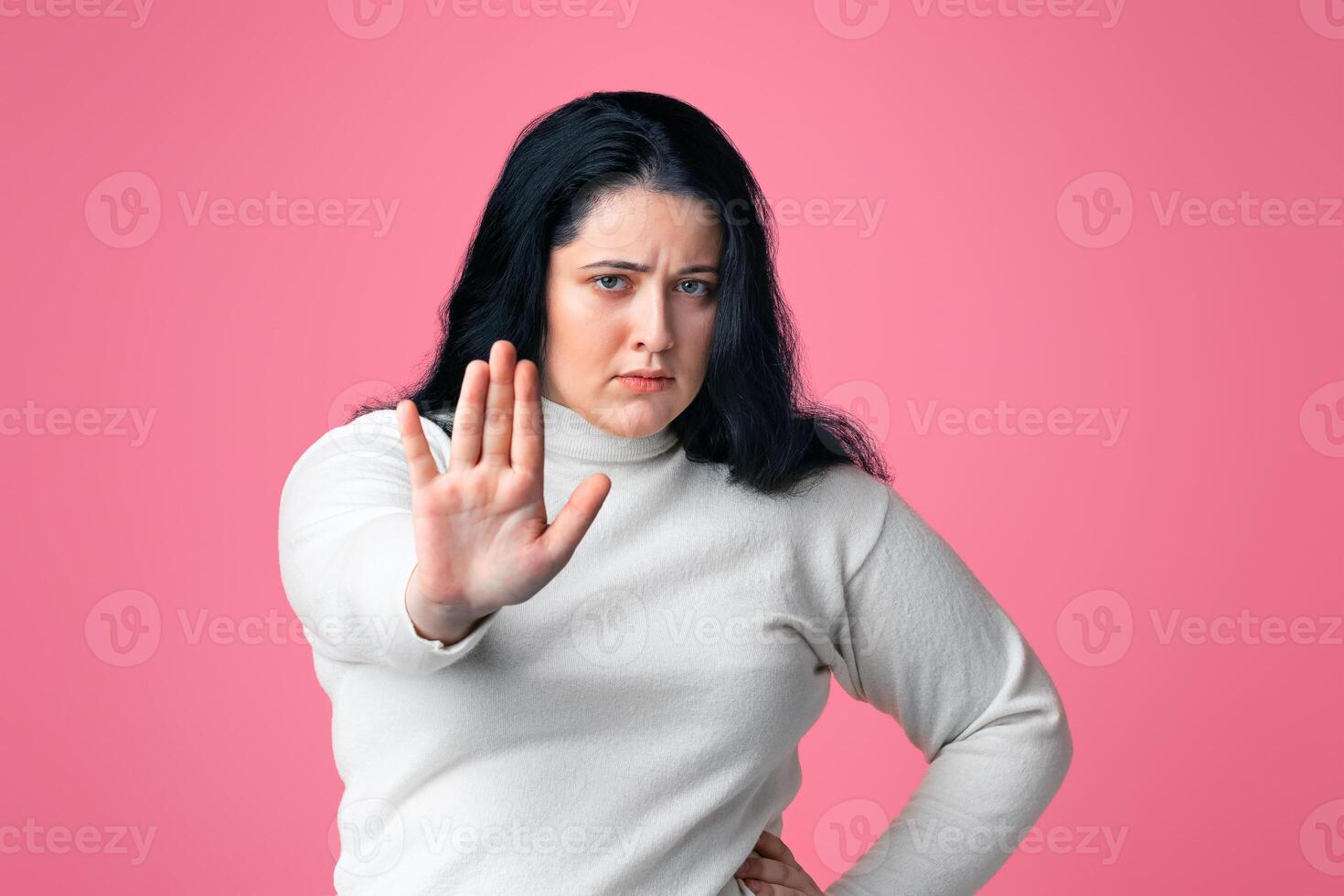 No Bullying Concept. Serious overweight girl showing stop gesture, standing with outstretched hand over pink background, copy space photo