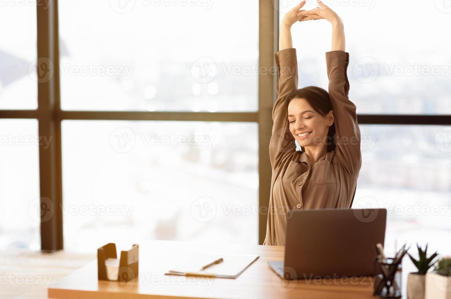 Relax At Work. Happy young woman sitting in modern office with pc, stretching her arms above her head and smiling photo