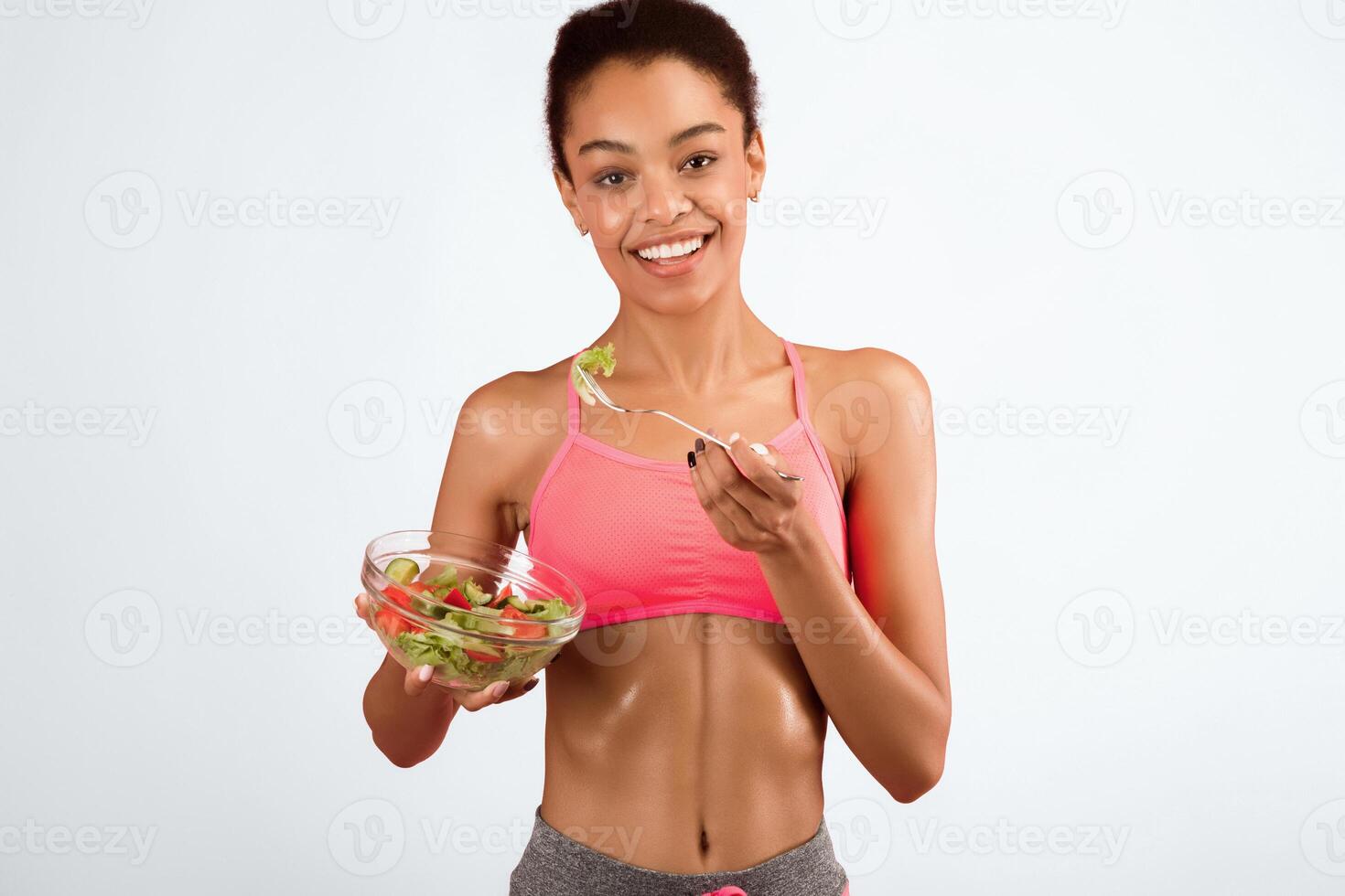 Sport And Nutrition. Fit Afro Girl Eating Vegetable Salad Standing Over Pink Background In Studio. photo