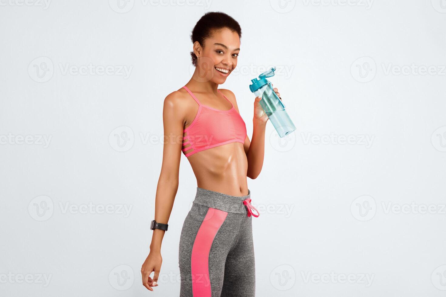 Fitness And Hydration. Slim African American Woman Holding Water Bottle Smiling At Camera On Pink Studio Background. Copy Space photo