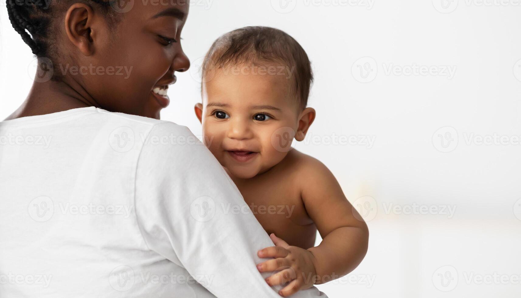 Happiness In A Smile. Portrait of adorable African American baby smiling, young mum holding and hugging her little child, playing together, white background, free copy space, banner, panorama photo
