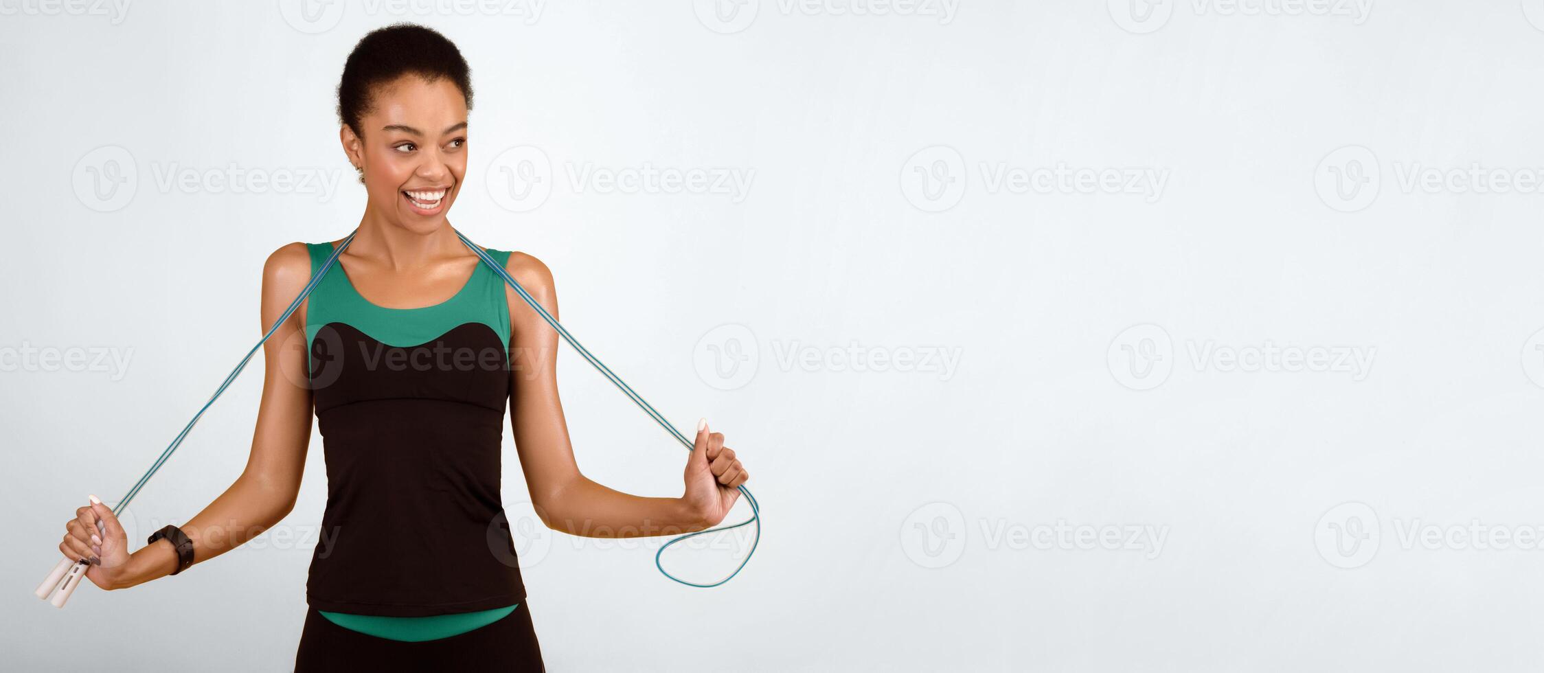 Sporty lifestyle. Happy black woman with jump rope smiling looking aside posing on yellow studio background. Empty space photo