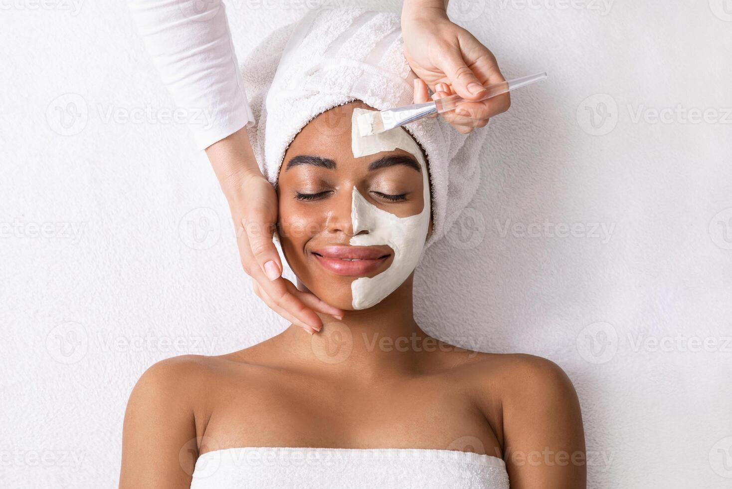 Black woman having white clay mask on half of her face, top view photo