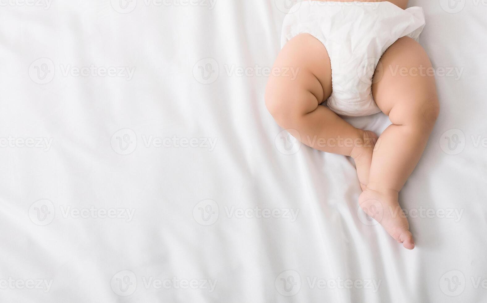 Baby legs and bottom in diaper on white bed background, top view, copy space photo