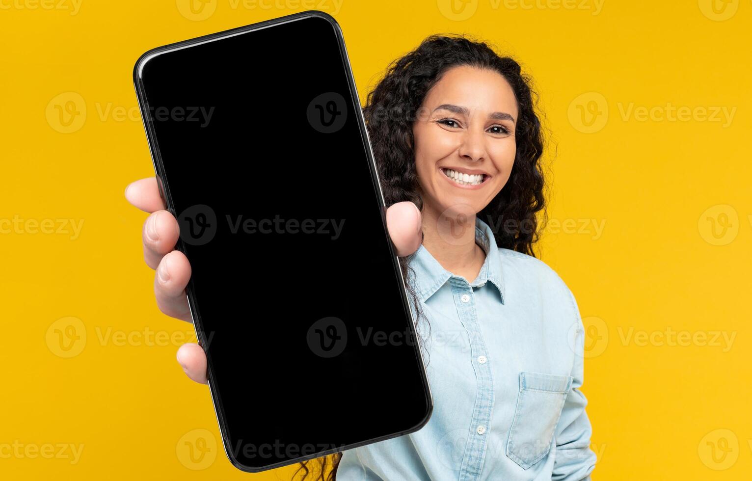 Check This Ad. Cheerful Woman Holding Big Blank Smartphone With Black Screen In Hand, Happy Millennial Lady Recommending New Application Or Mobile Website, Mockup Banner Collage, Yellow Orange Wall photo