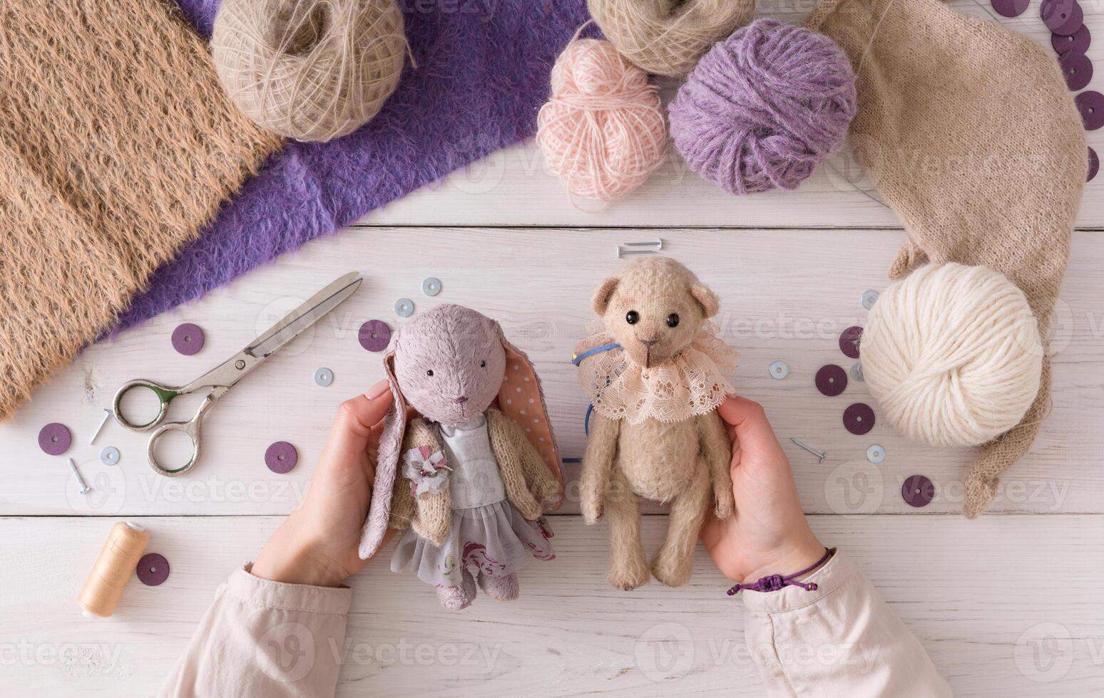 Process of making vintage toy, top view. Artisan pov, needlewoman hands holding handmade teddy bear and rabbit, home workshop photo