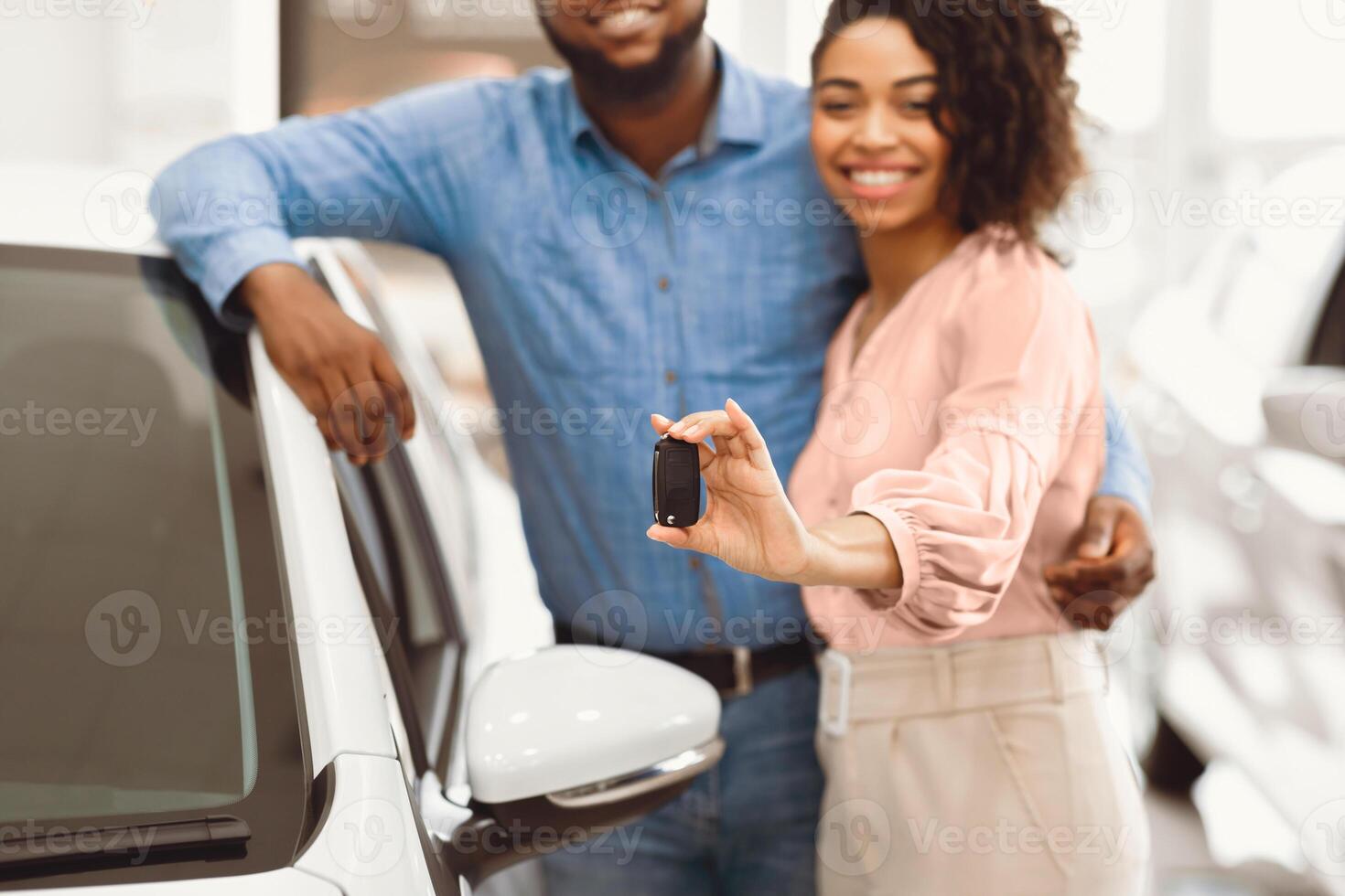 Own Car. Happy Black Couple Showing New Auto Key Embracing Standing In Dealership Store. Cropped, Shallow Depth photo