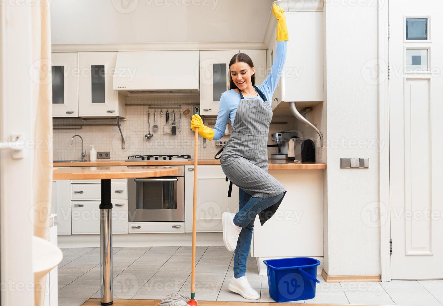 Having Fun. Carefree girl in yellow gloves cleaning kitchen floor, dancing with mop, copy space photo