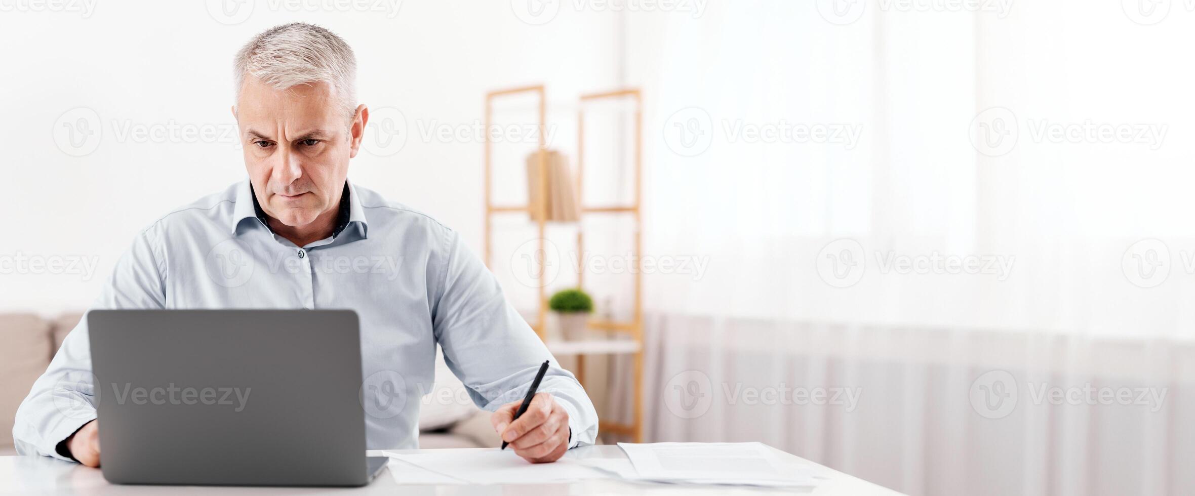 Budget Planning. Pensive Senior Man Using Laptop And Writing In Notebook Sitting At Desk At Home, Empty Space photo