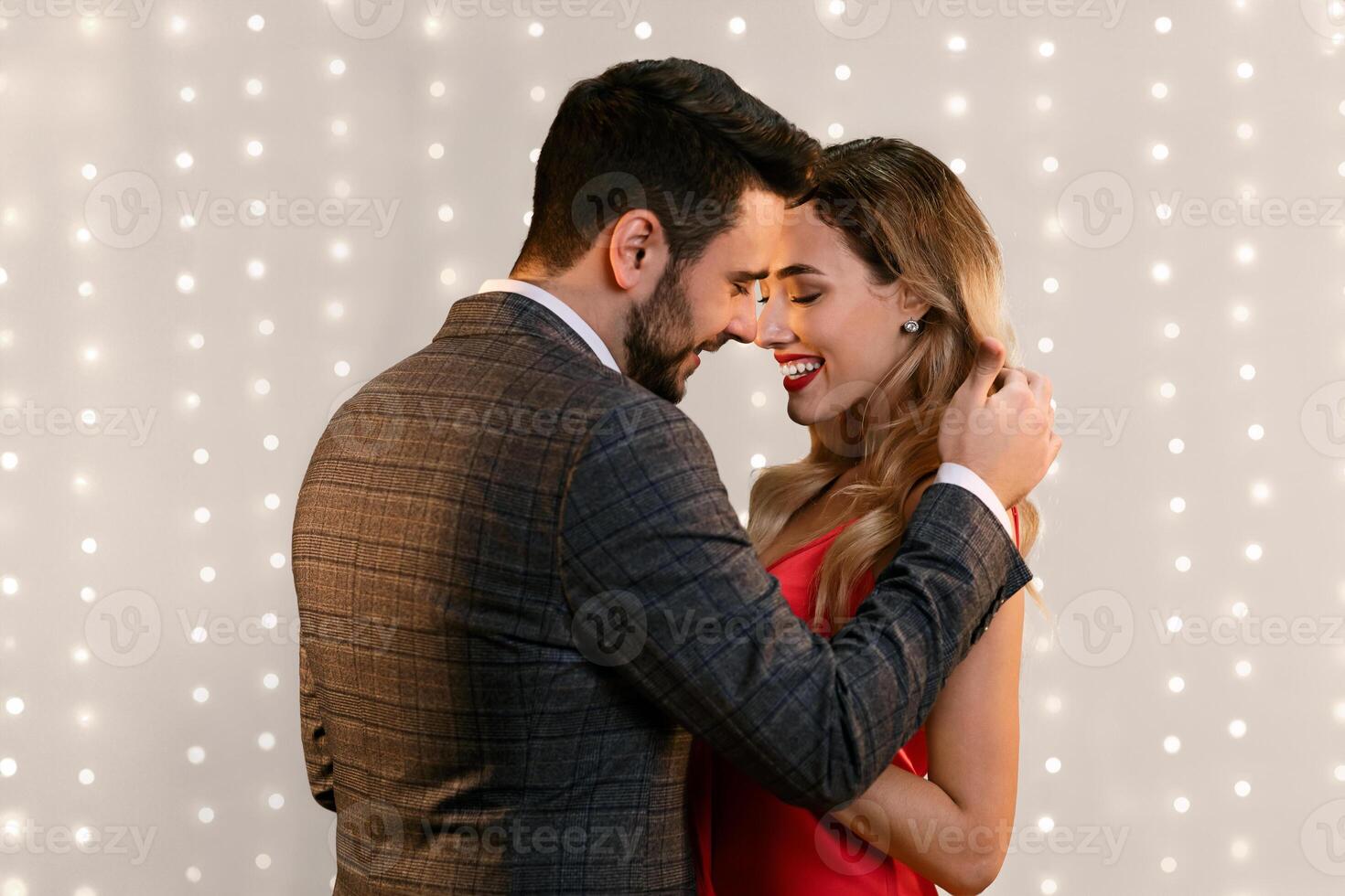 Tender Moments. Romantic man touching hair of his girlfriend, full of love and care while standing together over beige background with blurred lights photo