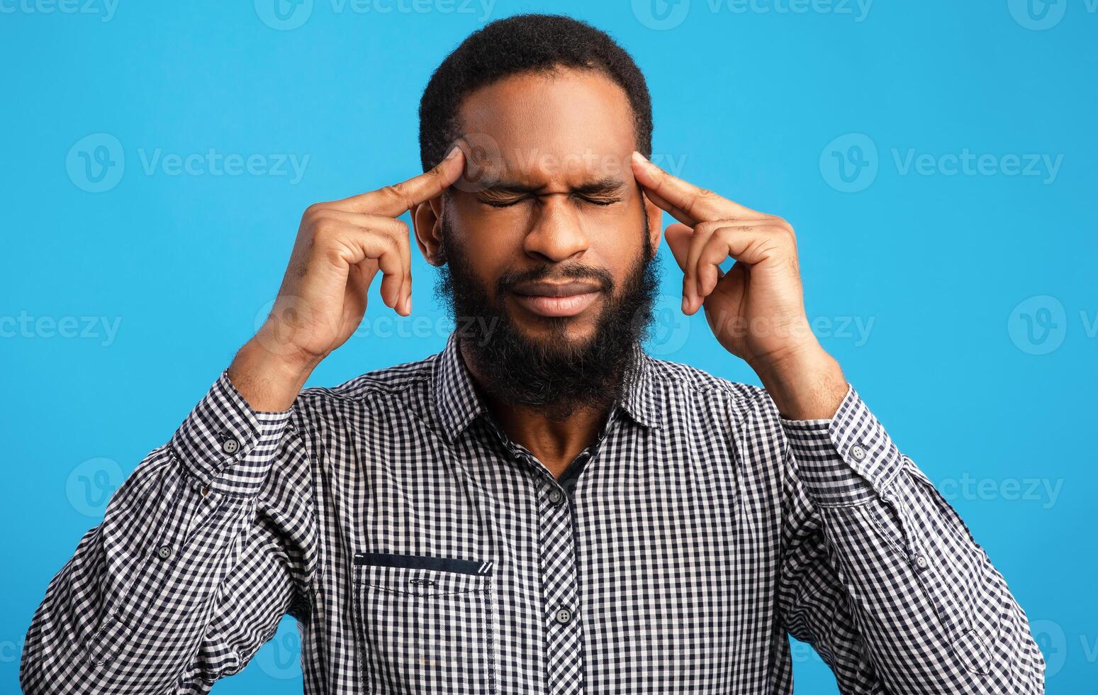 Portrait of thoughtful black guy thinking with closed eyes, touching temples with fingers, isolated over blue wall photo