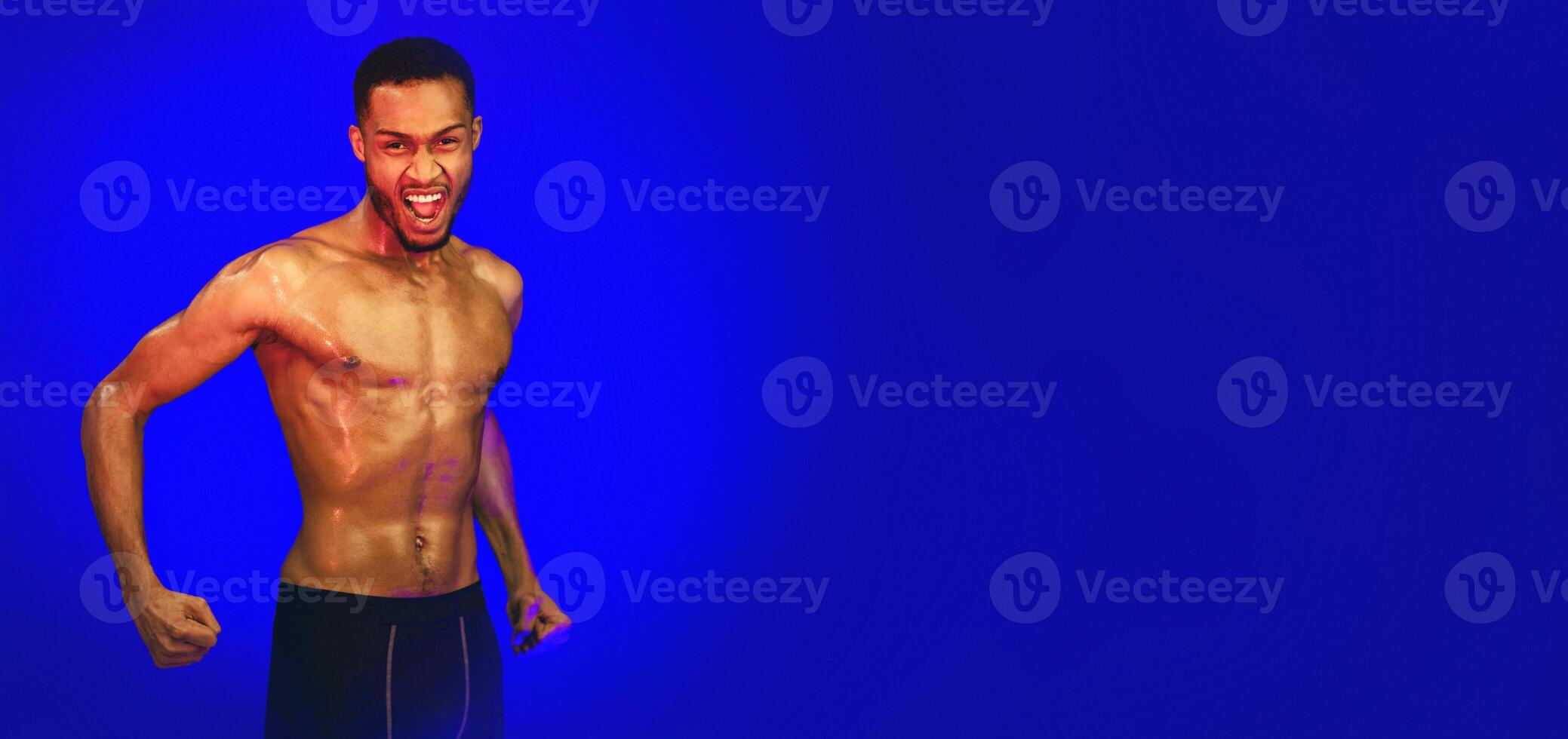Aggressive Shirtless Black Fighter Guy Shouting Clenching Fists Ready To Fight Posing On Blue Background. Studio Shot photo