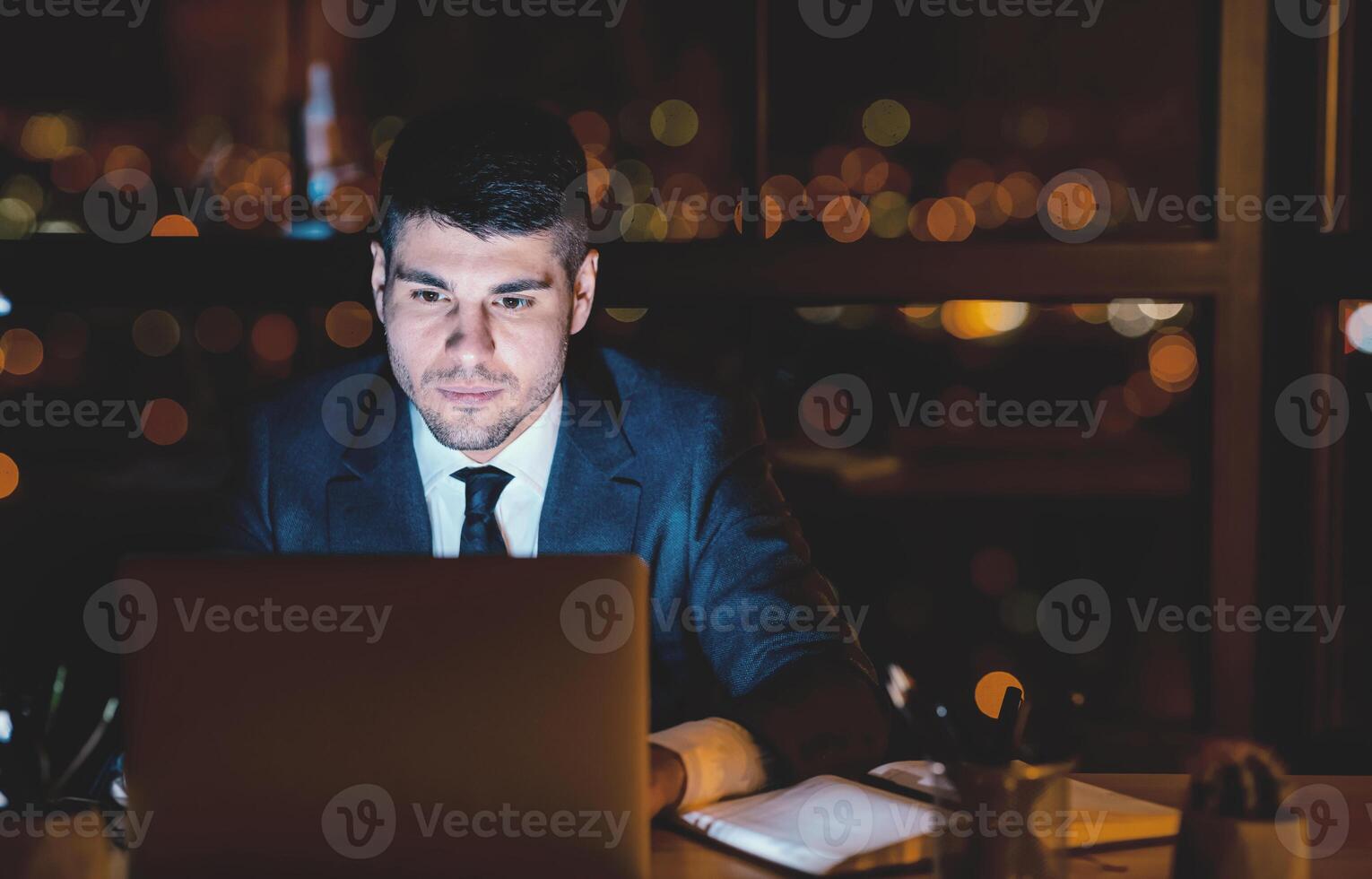 Business Man At Laptop Working Browsing Internet Overnight Sitting In Modern Office. Free Space, Selective Focus photo