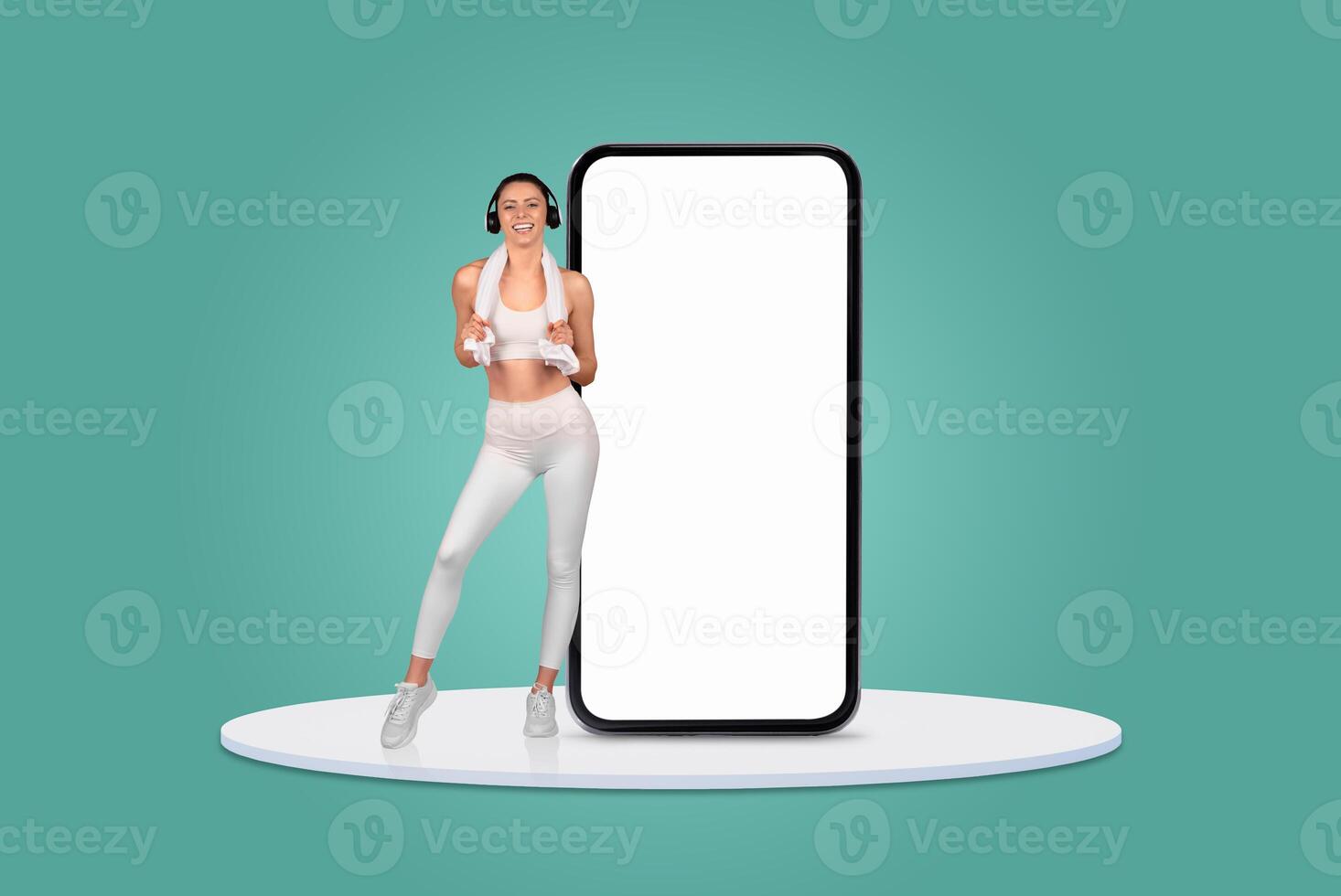 A woman in activewear is enjoying a dance workout while holding a game controller beside a large smartphone. She appears energetic and focused on her fitness routine. photo