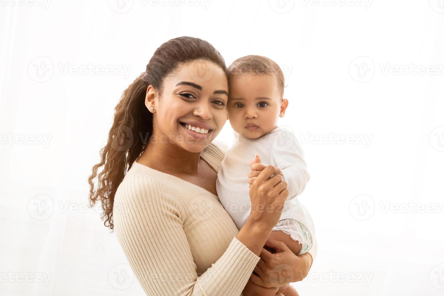 African Mother And Baby Portrait. Happy Black Mom Holding Her Adorable Little Infant Smiling To Camera Posing Standing Near Window Indoors. Joyful Motherhood Moments Concept photo