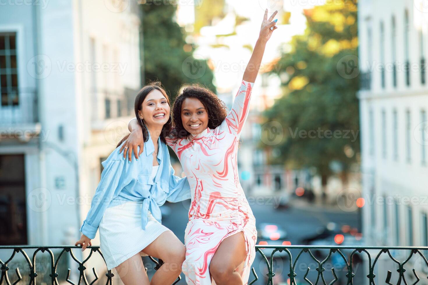 Two friends are happily posing together outdoors, celebrating their friendship in a vibrant urban setting as the sun lowers, casting a warm glow around them. photo