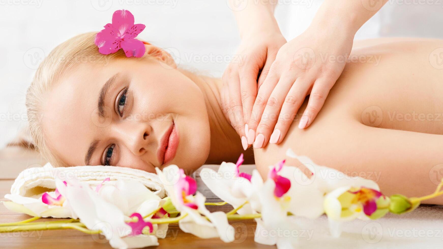 Relaxing in spa. Smiling girl lies on massage table, female hands massage shoulders, close up, free space photo