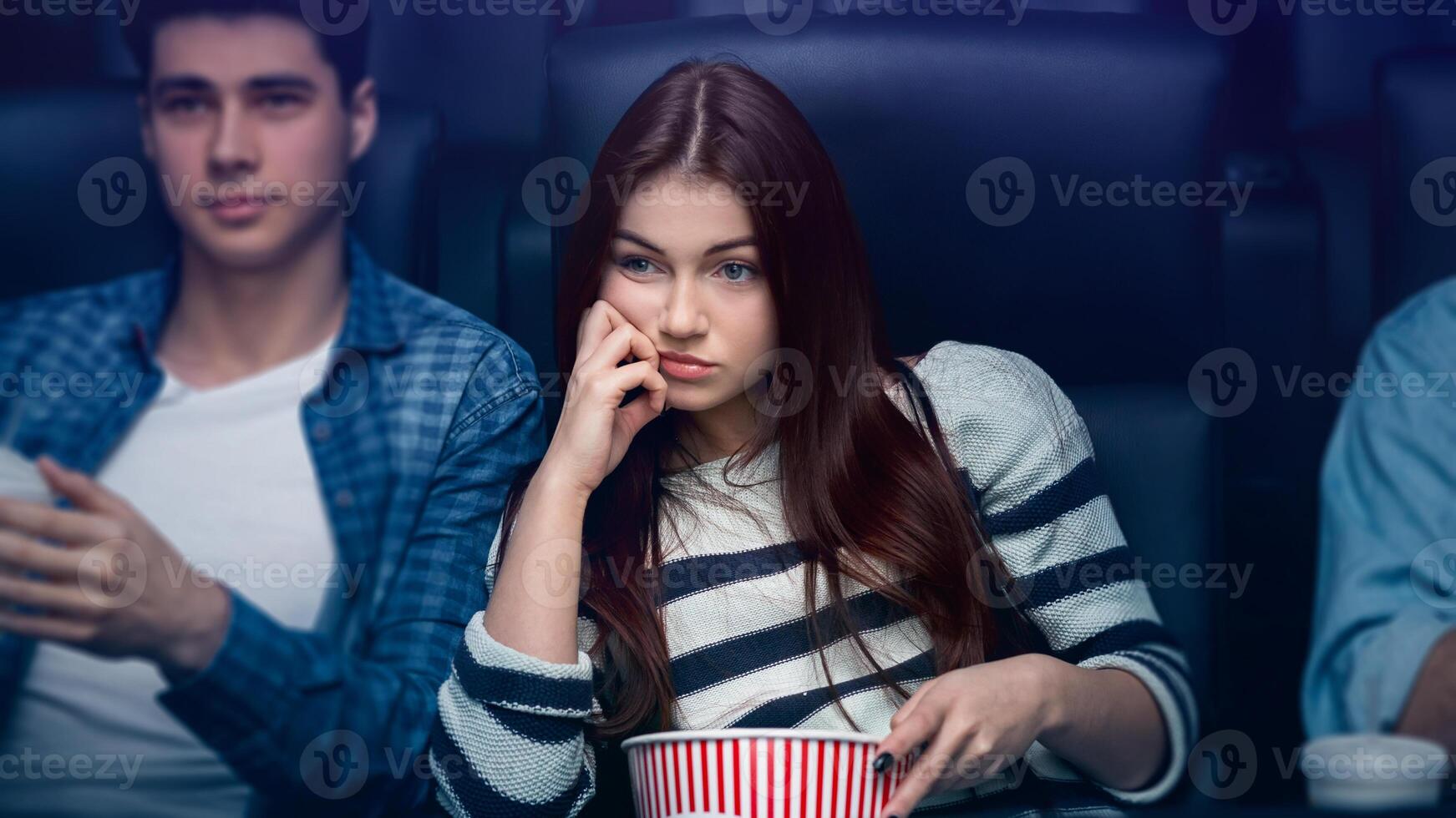 Boring date concept. Weary young girl with boyfriend watching movie in dark cinema photo