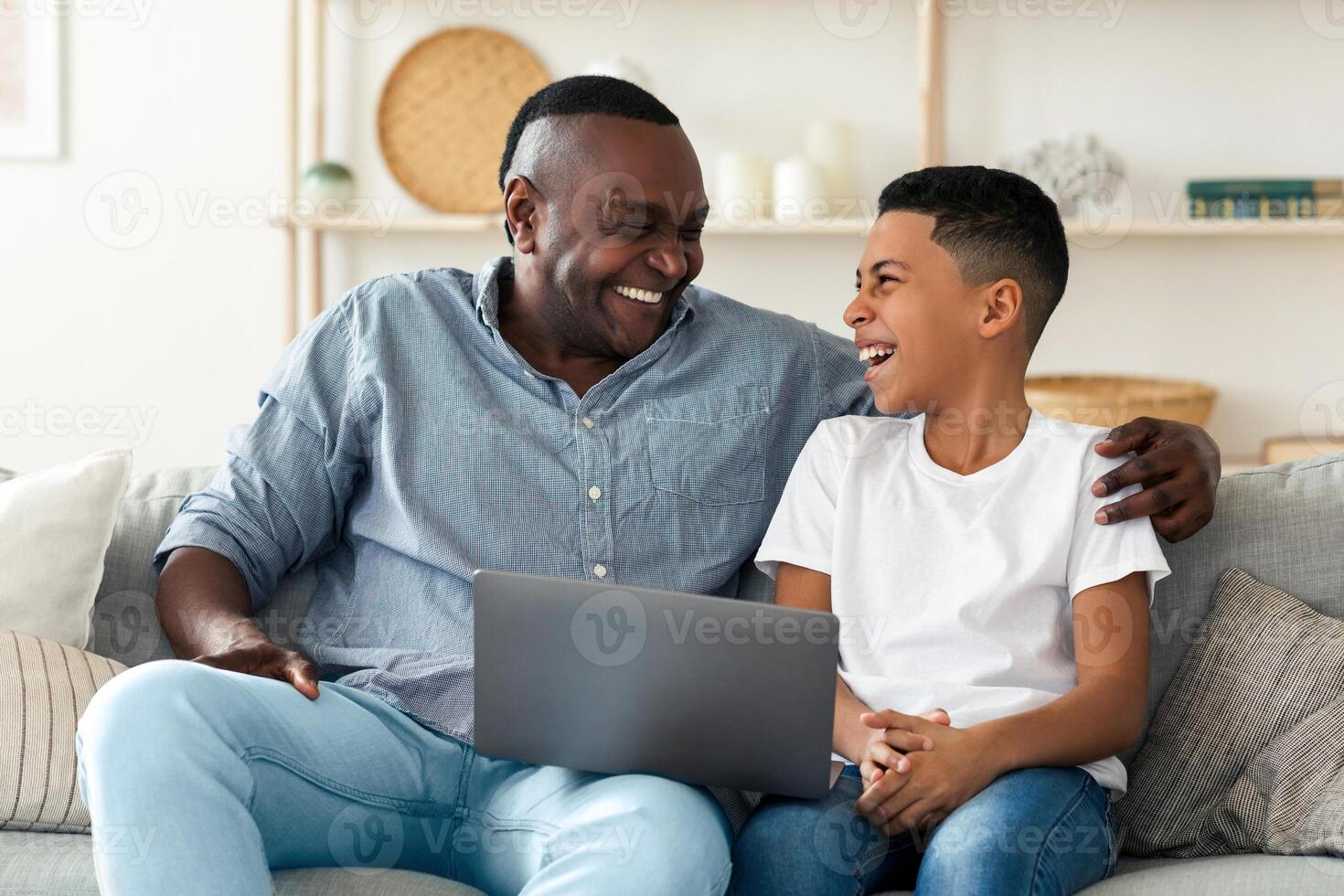 African Grandfather And Grandson Using Laptop Together Watching Comedy Movie At Home, Laughing And Hugging, Enjoying Time Together, Free Space photo