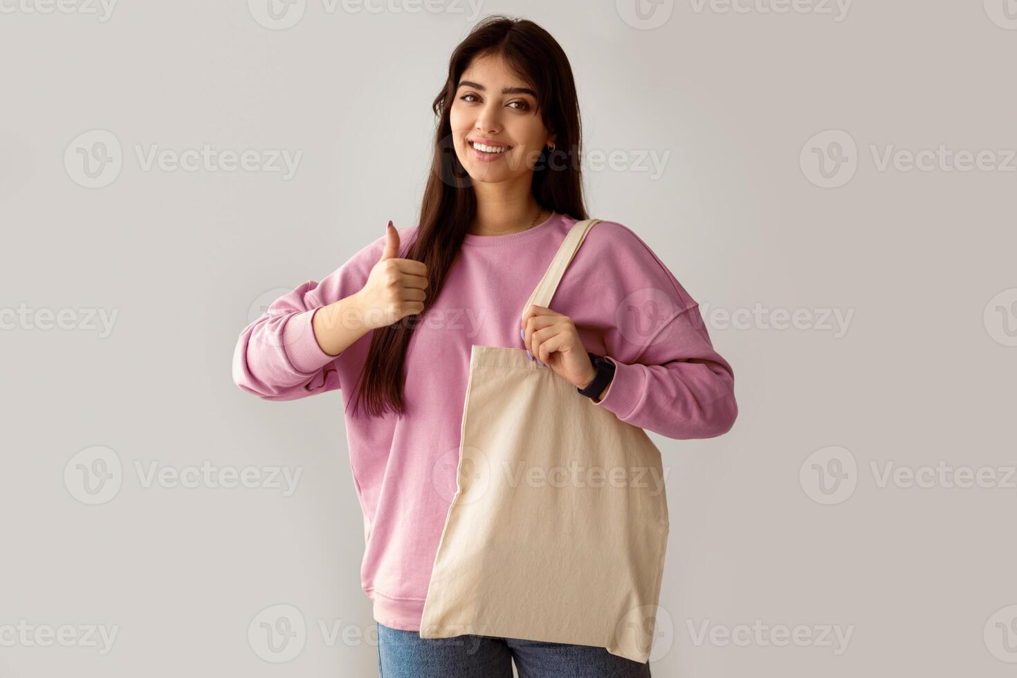 Zero Waste. Millennial Woman Showing Blank Eco Bag And Gesturing Thumbs Up Posing Standing On White Studio Background, Smiling To Camera. I Like Ecology Friendly Lifestyle, No More Plastic Concept photo