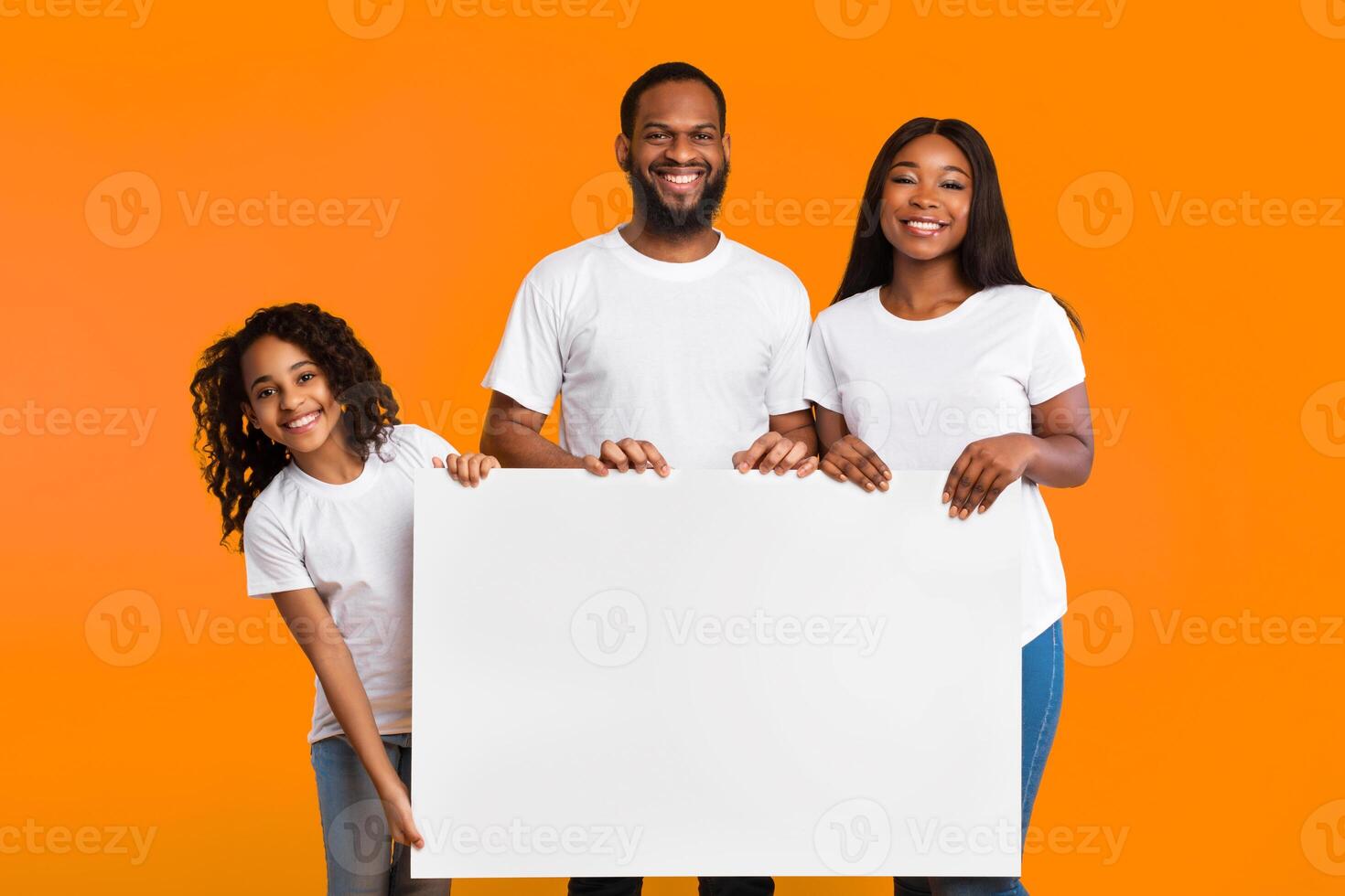 Cheerful Black Family Of Three Holding And Showing Blank Paper Poster For Your Text Smiling To Camera Standing Isolated Over Yellow Studio Background. People With White Square Board For Advertising photo