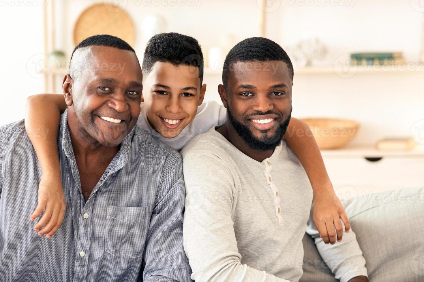 Happy african boy hugging his father and grandpa while posing to camera at home, bonding together, free space photo
