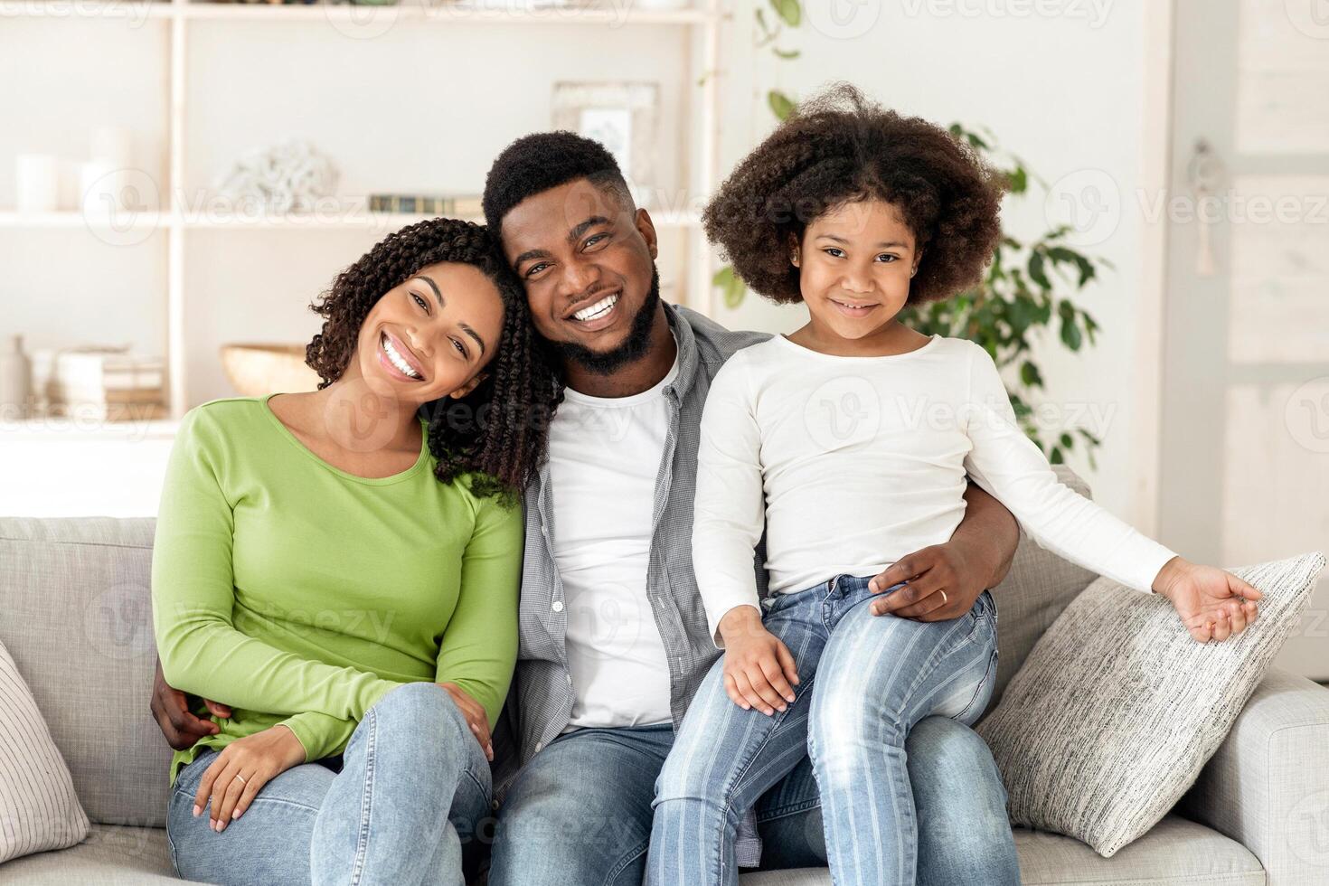 Family Insurance Concept. Portrait Of Happy Black Father, Mother And Little Daughter Posing On Couch At Home photo